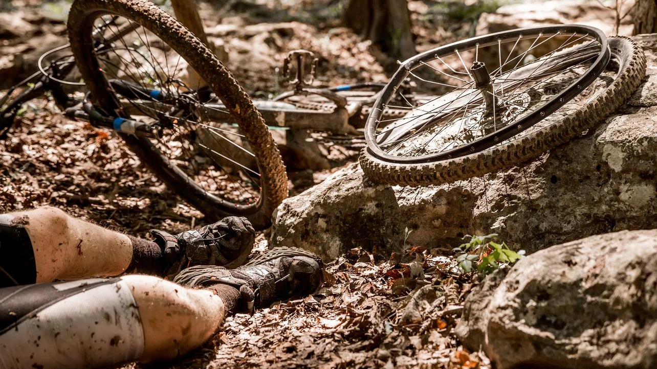 A mountain biker has an accident on his bike.