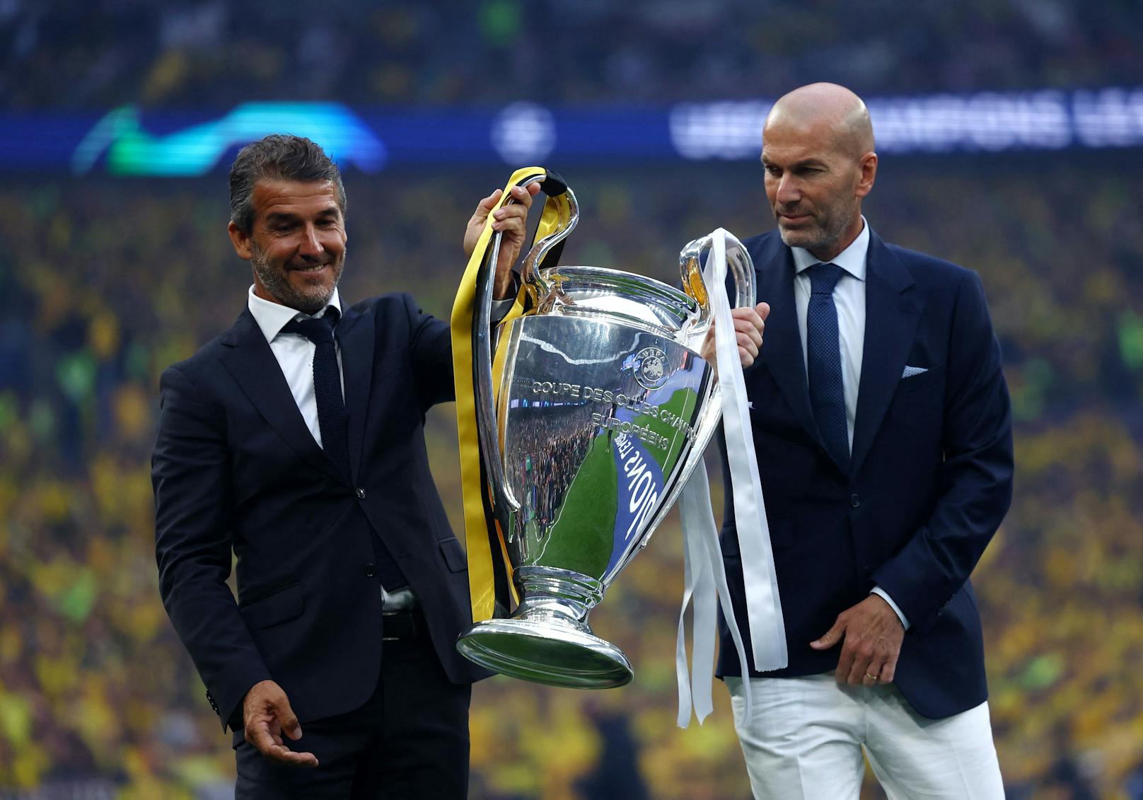Karl-Heinz Riedle und Zinedine Zidane bringen den Champions-League-Pokal auf den Rasen. 