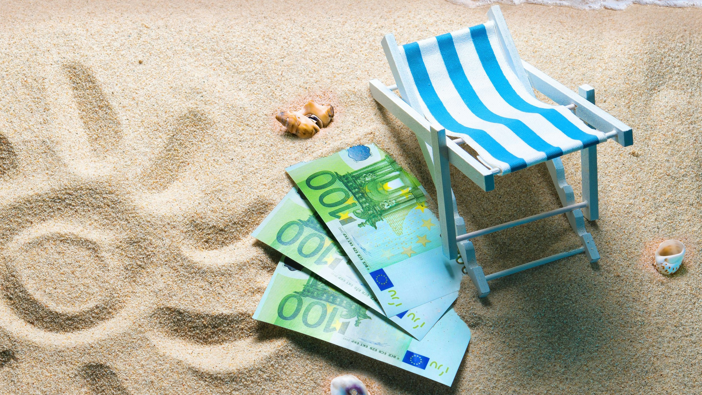 Deckchair with euro bills on a beach with a sun drawn on the sand. Travel money savings concept