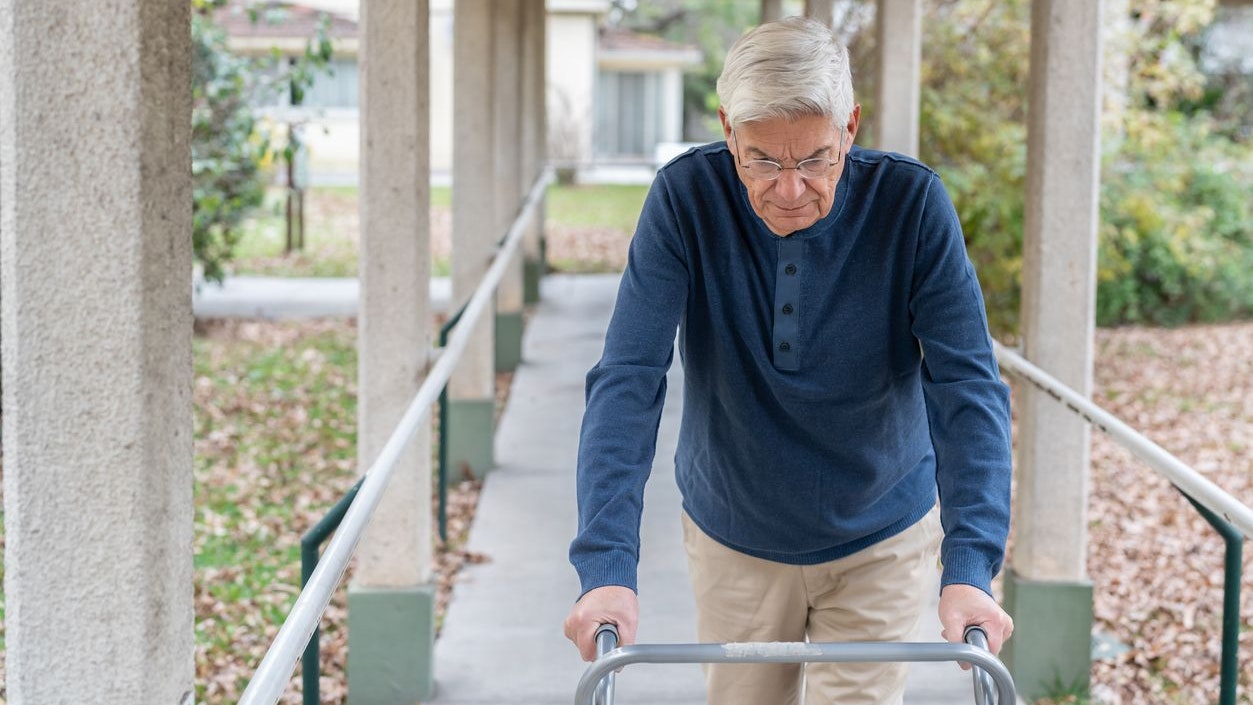 Focused senior man at a retirement home walking on the outside corridors with the help of a mobility walker - Lifestyles