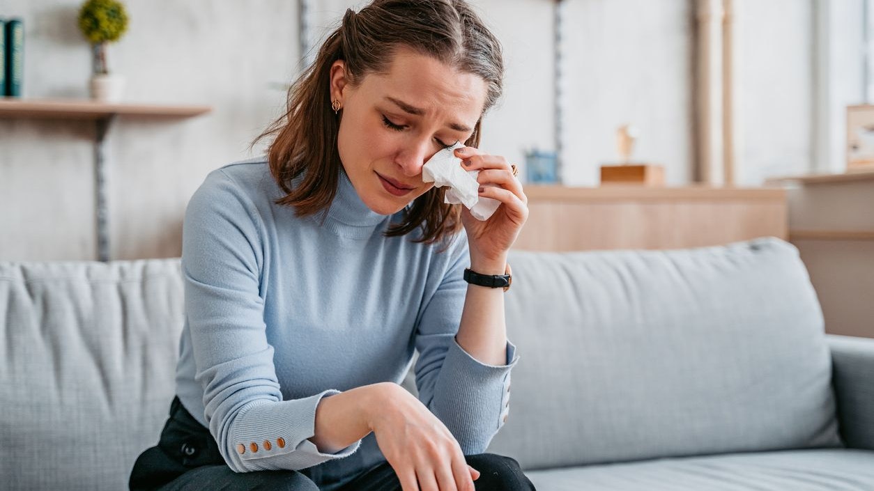 Beautiful young woman sitting on the sofa in the living room and crying.