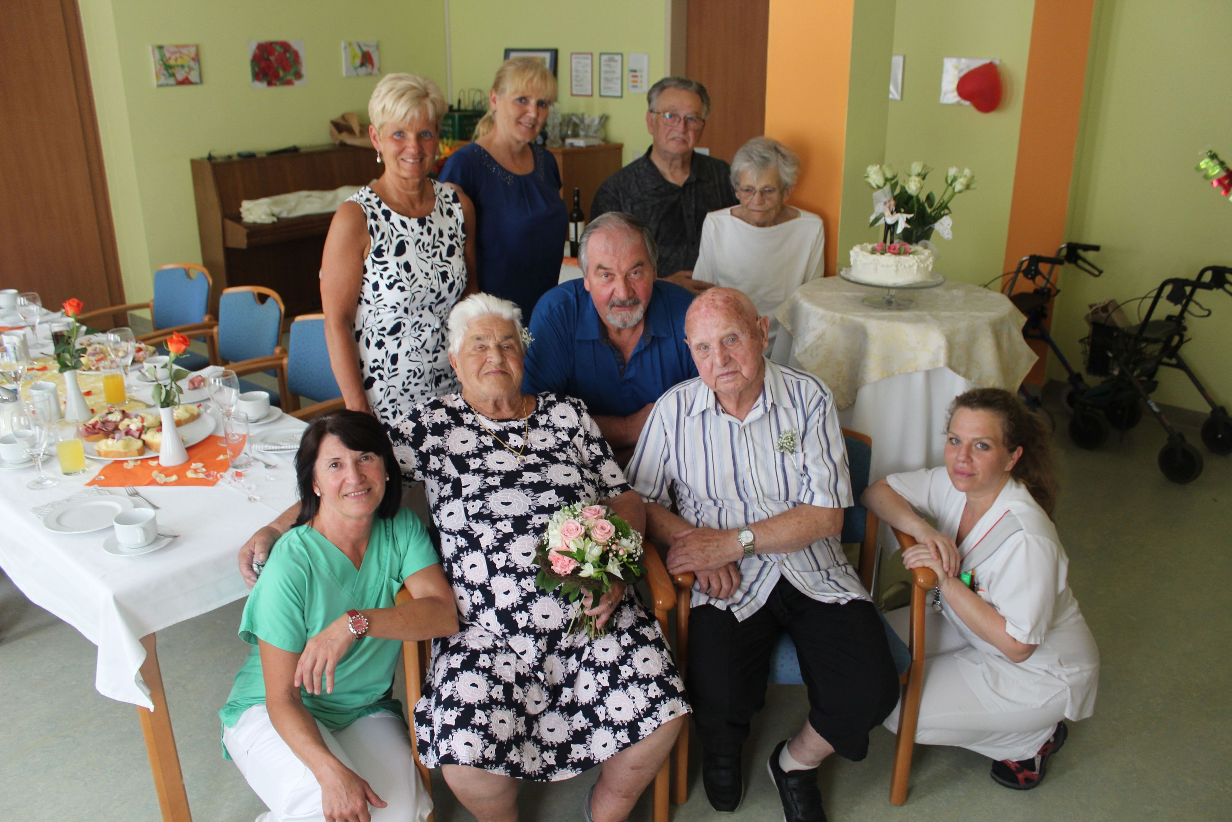 Das glückliche, gesegnete Paar im Kreis der Gratulantinnen und Gratulanten 1. Reihe v.l.: Managerin Ehrenamt & Alltagsbegleitung Elisabeth Schönhofer; Alice Auer; Sohn Johann Auer; Othmar Ziegler; Pflege- und Betreuungsmanagerin Michaela Lehocky; 2. Reihe v.l.: Stadträtin Elisabeth Schüttengruber-Holly; kaufmännische Direktorin Regina Maria Berger, Diakon Heribert Auer; Gertrude Auer