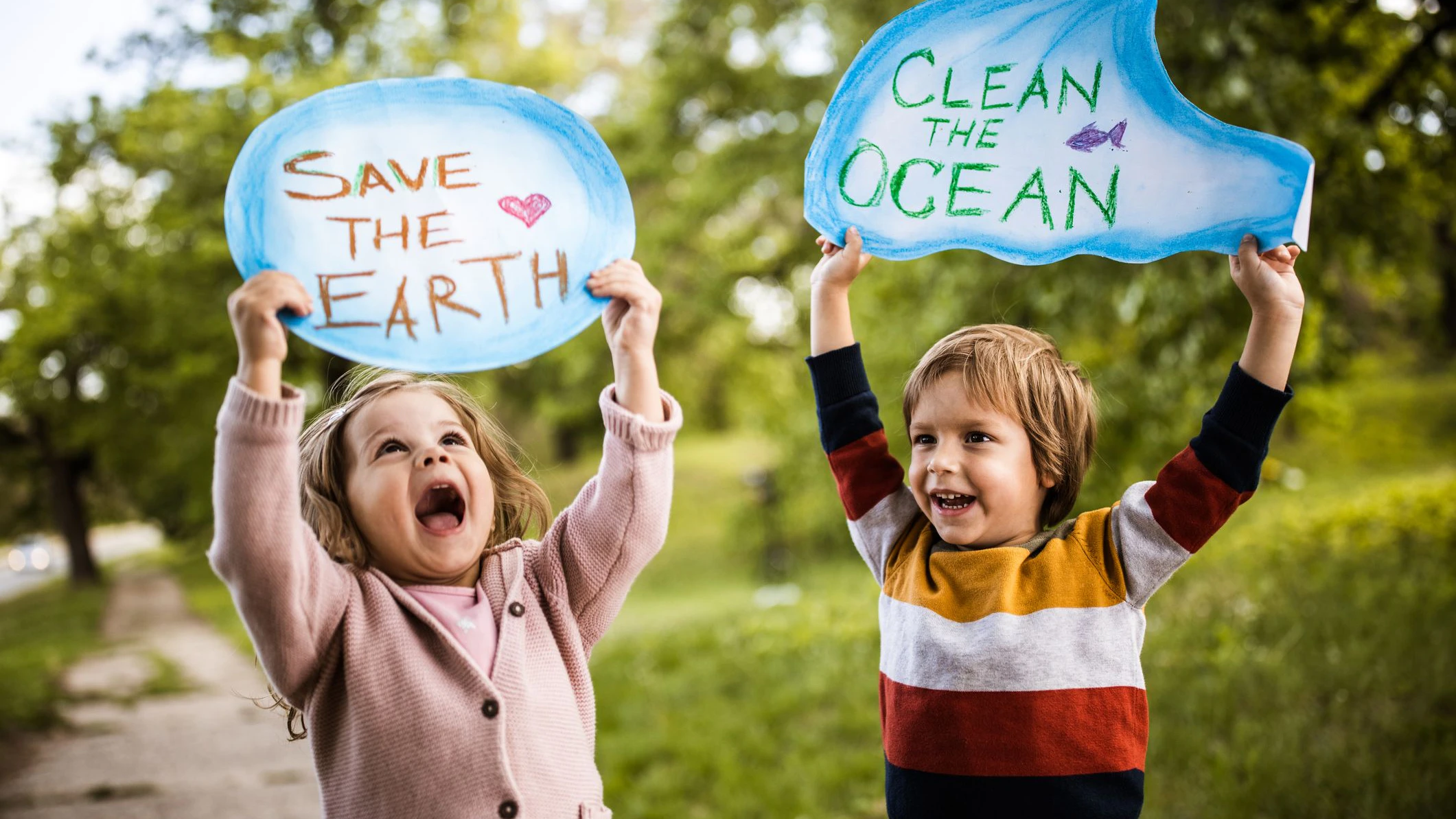 Happy kids holding placards for environmental conservation at the park. Focus is on boy.