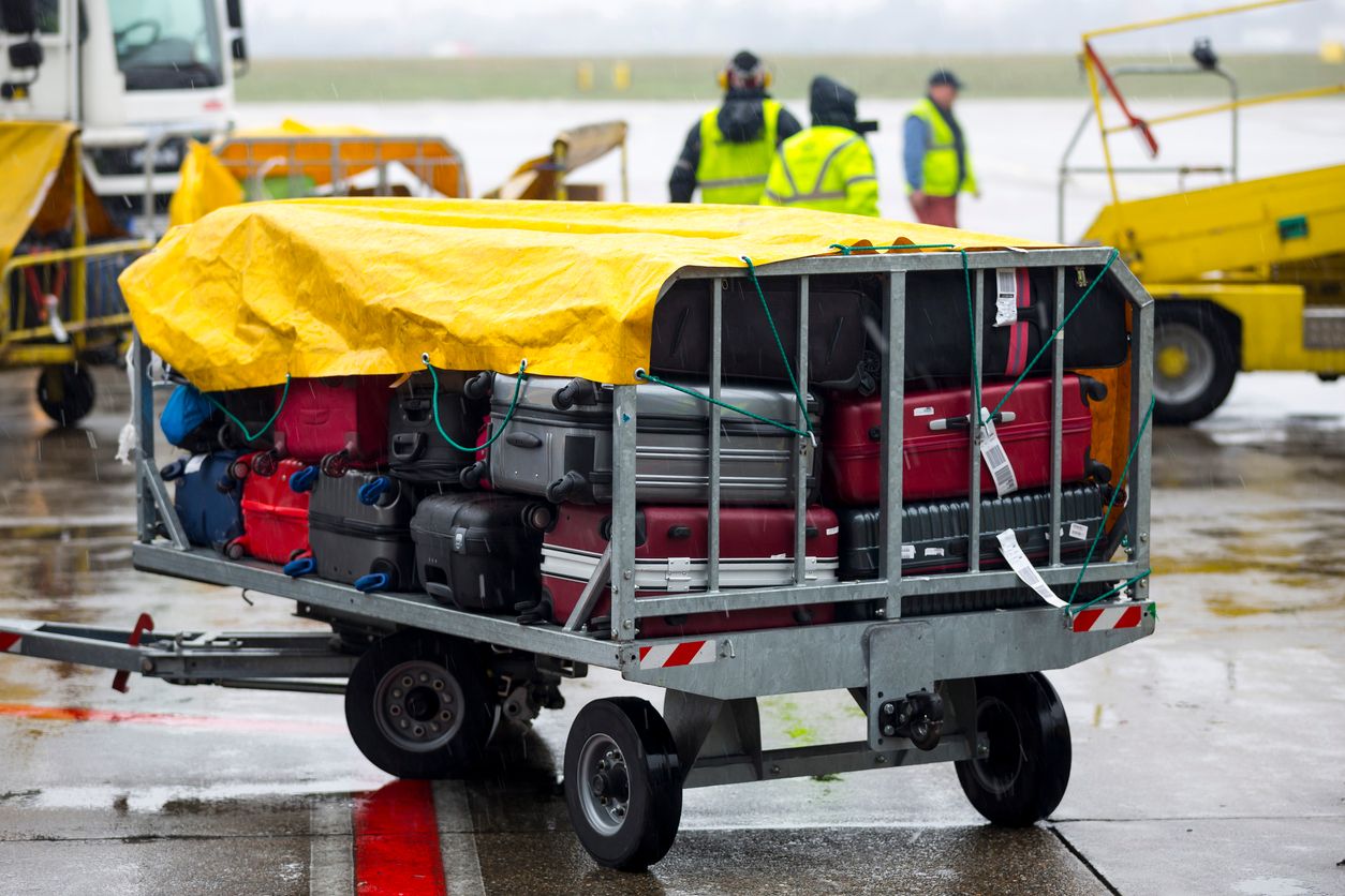 Passengers' luggage is seen covered from the rain on a cart near the airplane.