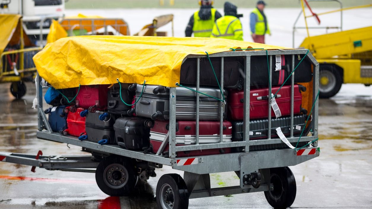 Passengers' luggage is seen covered from the rain on a cart near the airplane.