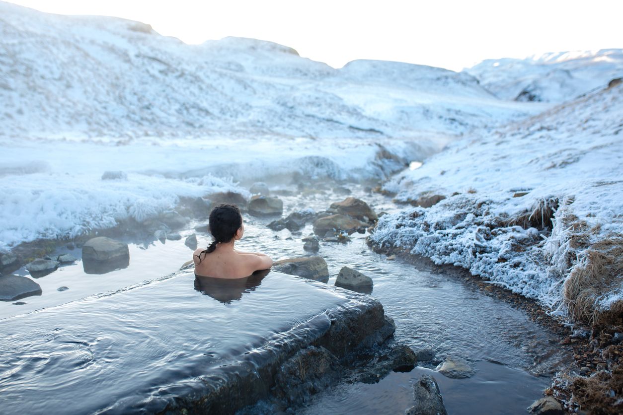 Auf Island kann man in heißen Quellen baden, während man den Blick auf die verschneiten Berge genießt.