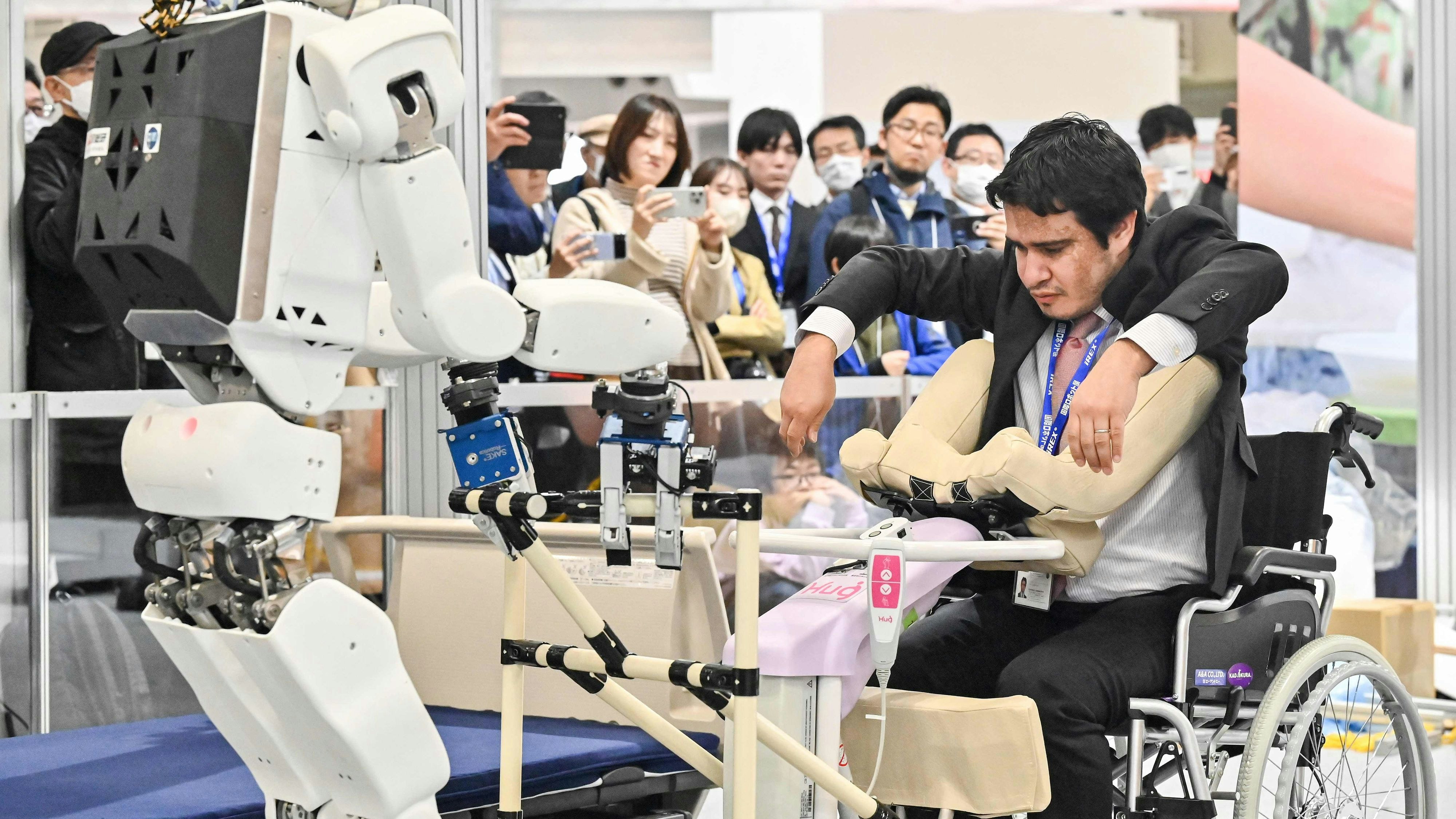 Ein hochspezialisierter Roboter des Herstellers Kawasaki hilft einem Mann mit Handicap in seinen Rollstuhl: Vorführung auf der Internationalen Roboter Ausstellung im November 2023 in Tokio