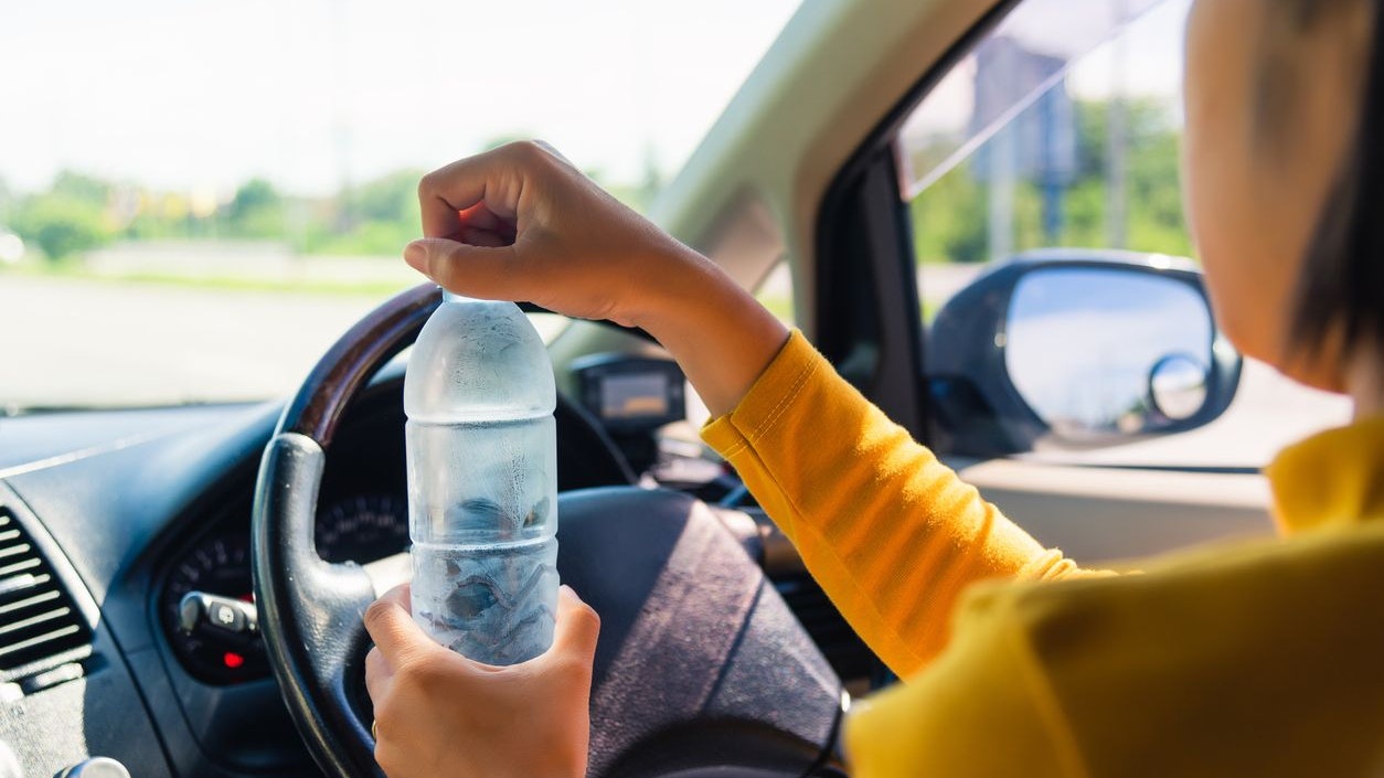 Asian woman holding a water bottle for drink while driving the car in the morning during going to work on highway road, Transportation and vehicle concept