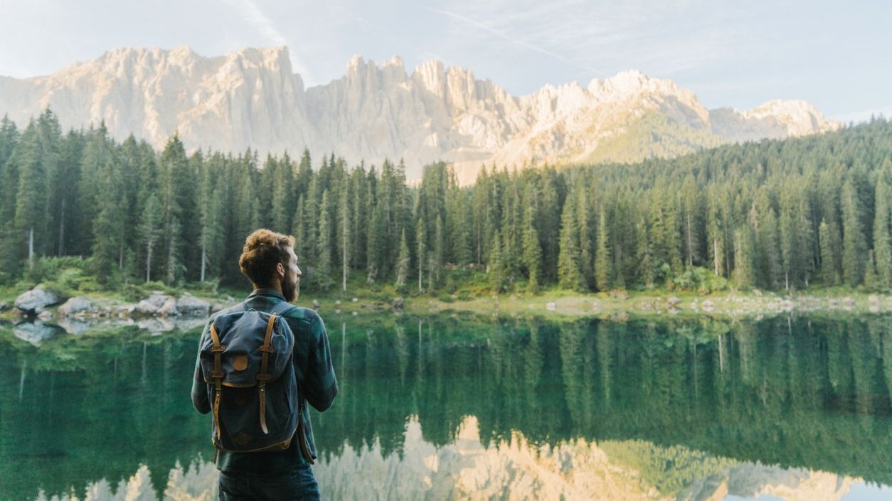 Young Caucasian man standing and looking at  Lago di Carezza in Dolomites