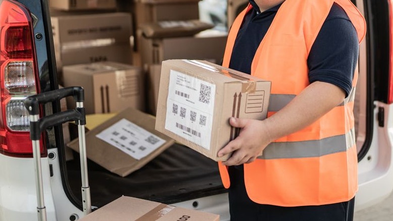 Porträt eines Mitarbeiters mit besonderen Bedürfnissen, der Kartons im Freien bestellt. Symbolbild. 