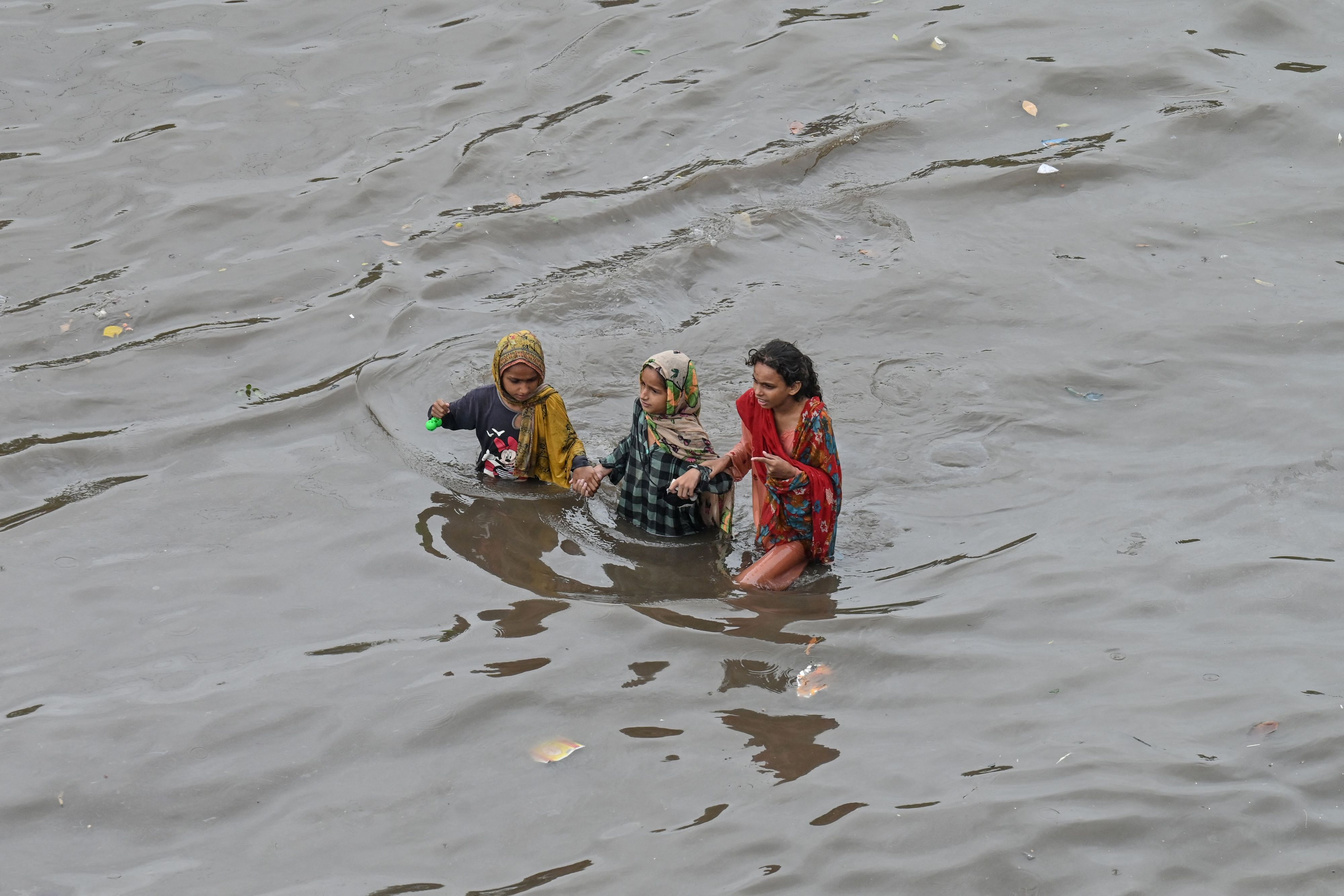 Drei Mädchen waten auf einer überschwemmten Straße in Lahore durch die Fluten.