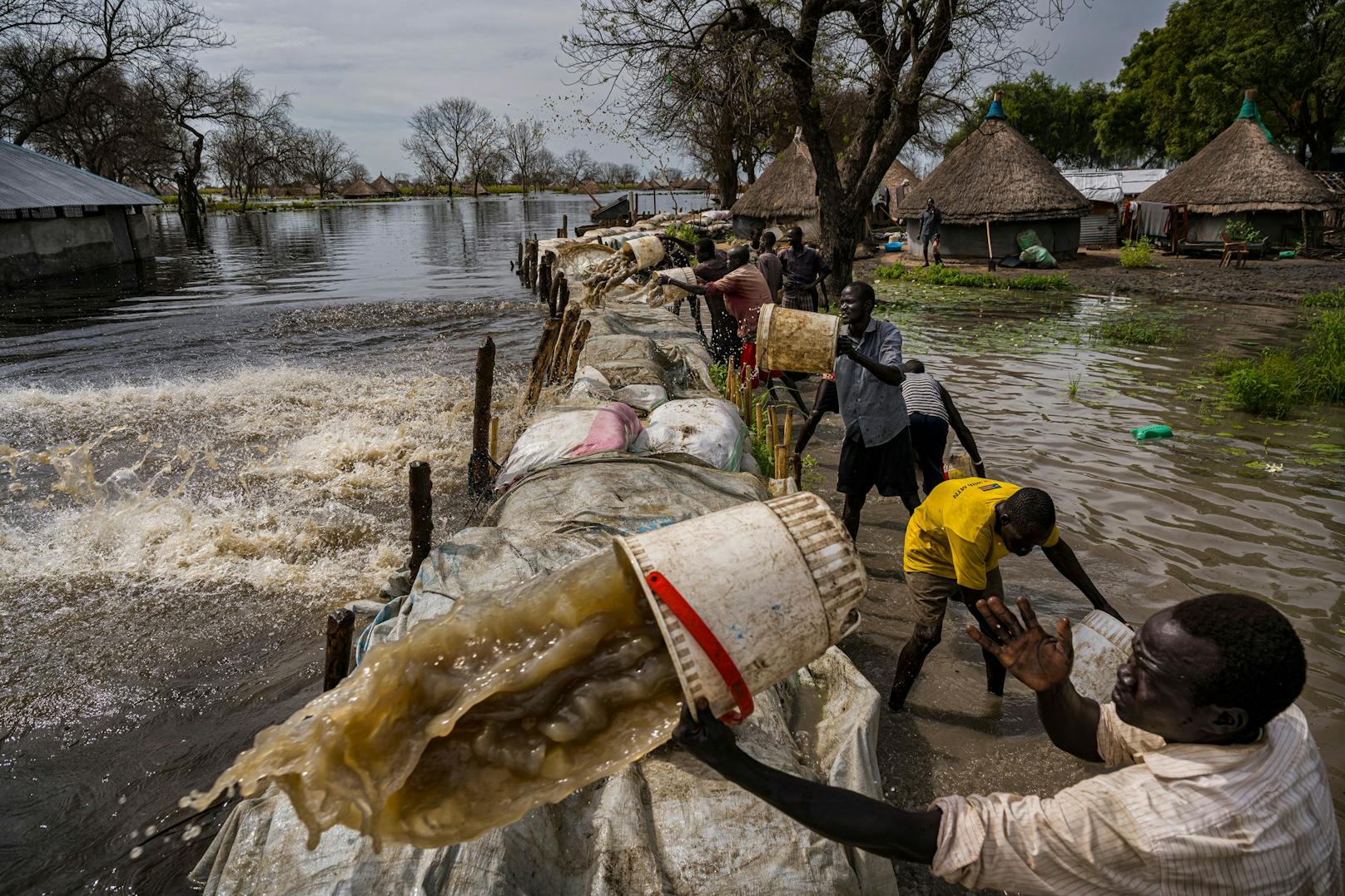 Männer verwenden Kübel, um Regenwasser in Paliau (Südsudan) über einen Damm zu schütten.