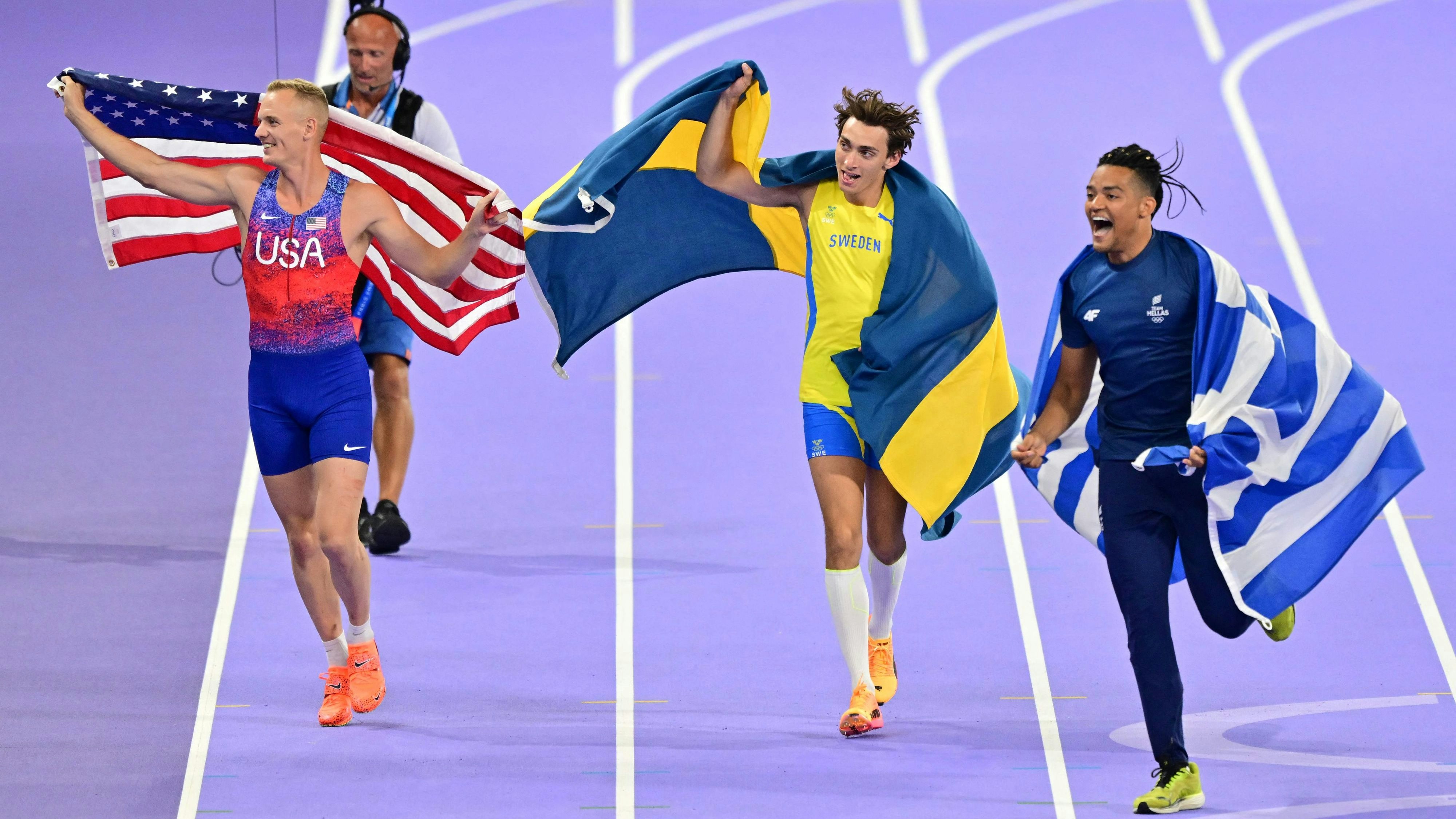 Goldmedaillengewinner und Weltrekordhalter Armand Duplantis mit dem Amerikaner Sam Kendricks, der Silnber holte, und dem drittplatzierten Griechen Emmanouil Karalis auf ihrer Ehrenrunde durch das Stade de France