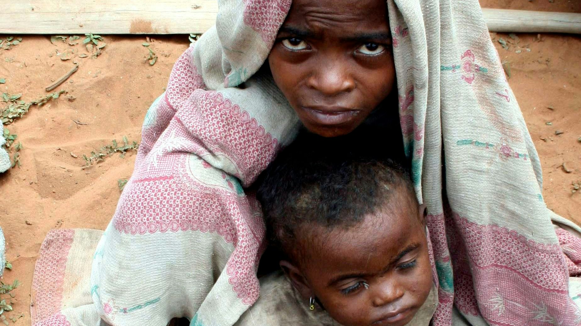 A Malagasy boy shelters his younger brother from the heat of the drought-affected Anosy region while their mother lines up for food aid at a therapeutic feeding centre for children in Amboassary, southern Madagascar January 15, 2007. Picture taken January 15, 2007.  REUTERS/Jasleen Sethi   (MADAGASCAR)