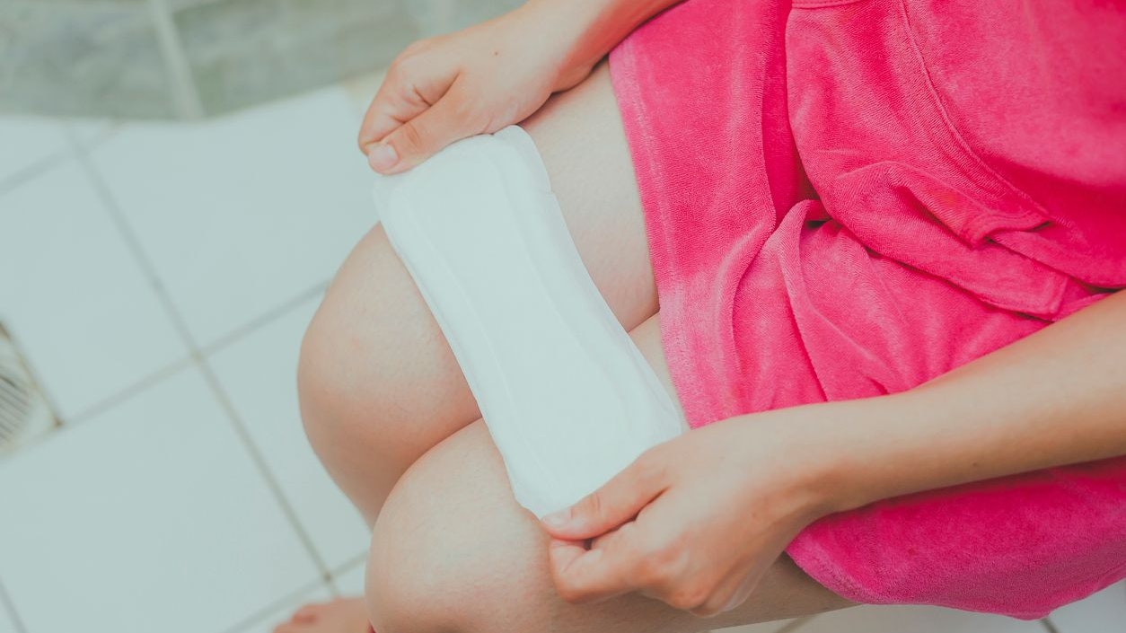 Woman in a toilet with a sanitary napkin. Young girl holds a sanitary pad while sitting in the toilet