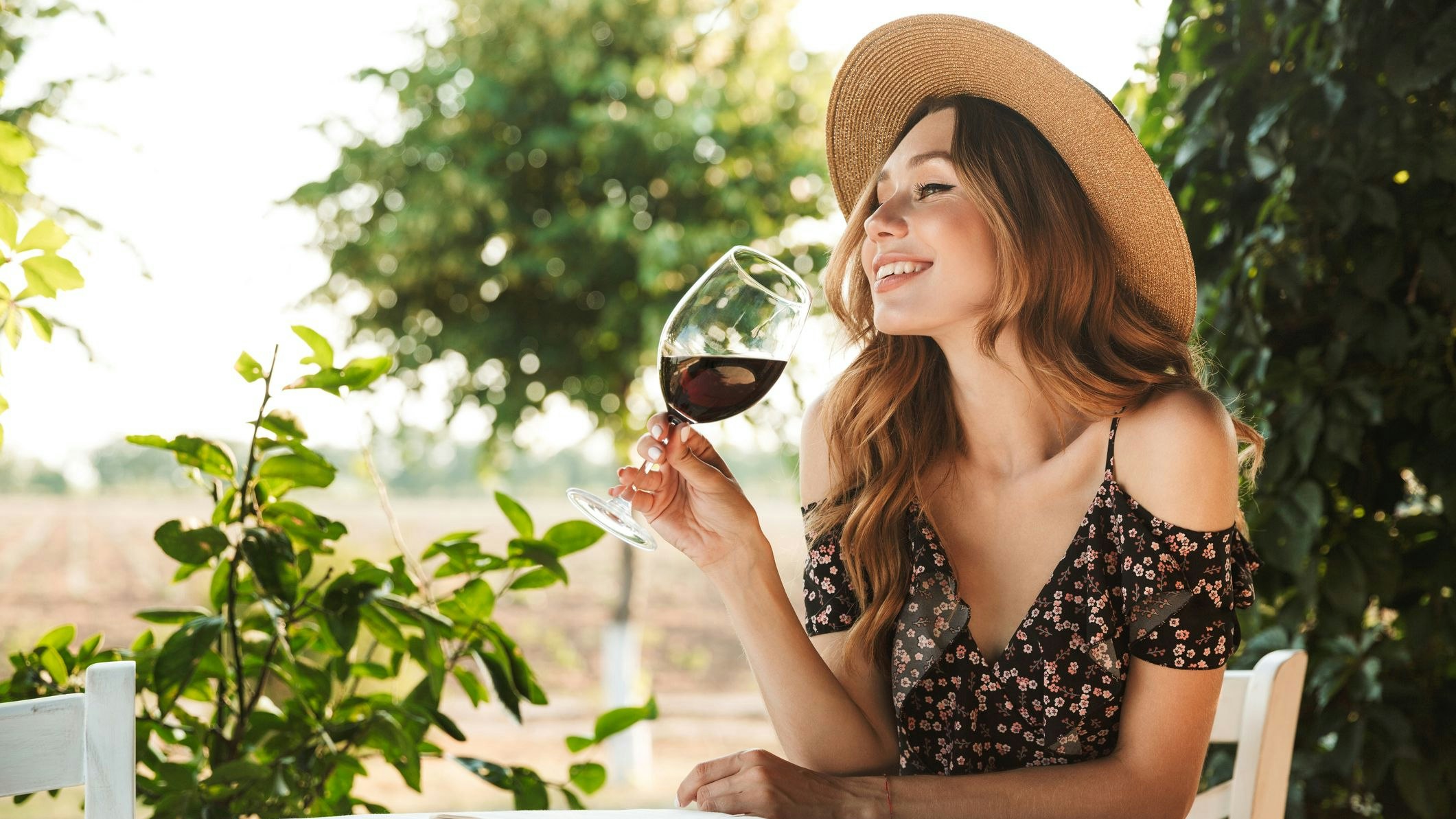 Image of cute pretty young woman sitting in cafe outdors in park with book holding glass drinking wine.