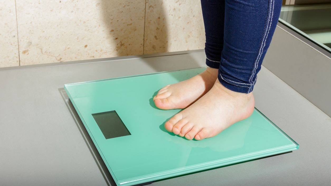 Child's foot is standing on modern floor scale measuring her weight.