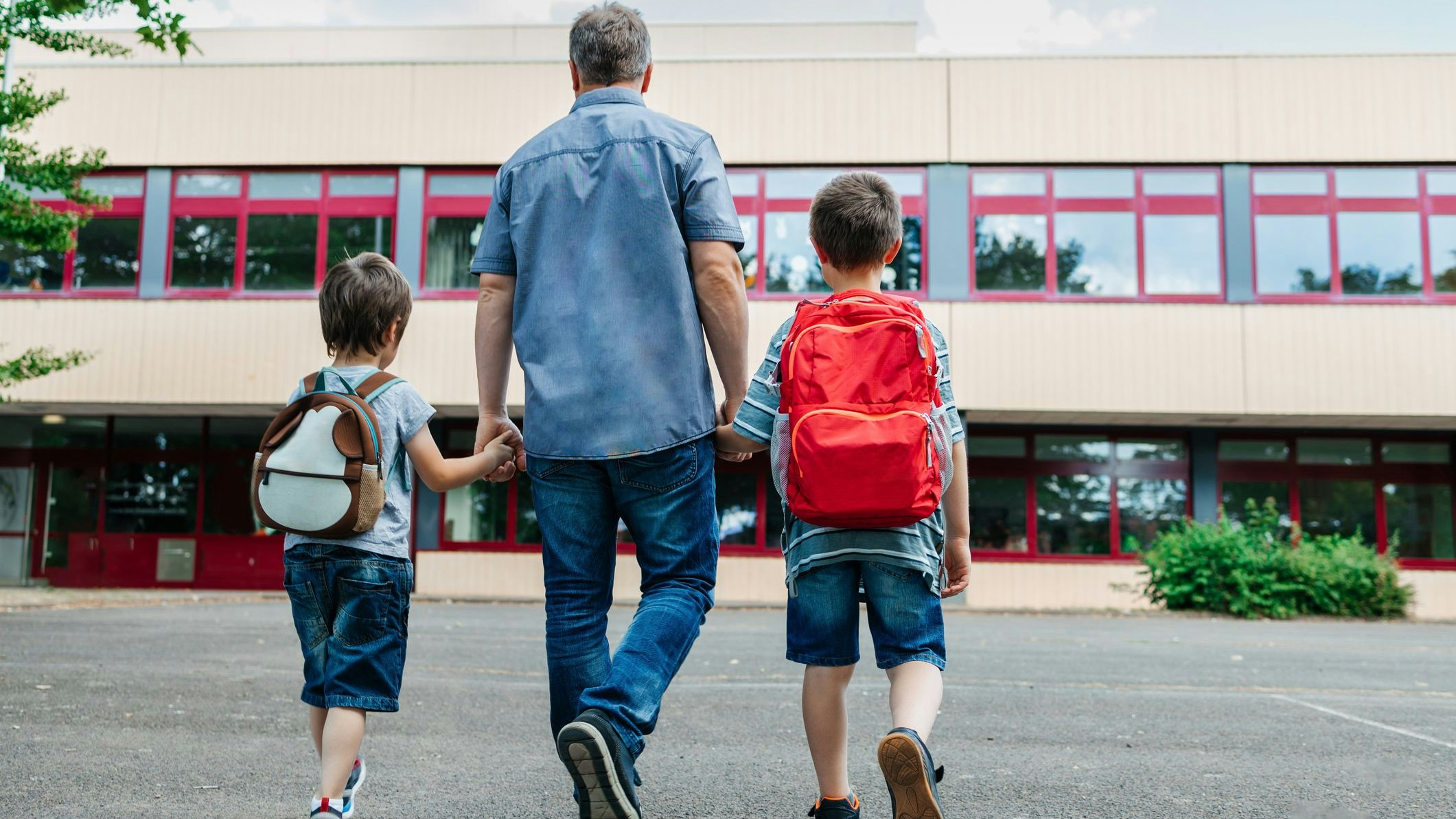 Back to school. View from the back of a happy dad escorts his sons schoolchildren to school. Parental care for children.