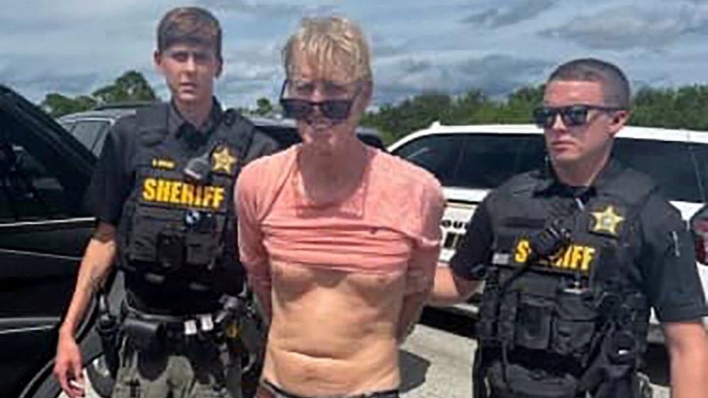 Ryan W. Routh, suspected of attempting to assassinate Republican presidential nominee and former U.S. President Donald Trump at his West Palm Beach golf course, stands handcuffed between two Martin County Sheriff's office deputies after his arrest during a traffic stop near Palm City, Florida, U.S., September 15, 2024.  Martin County Sheriff's Office/Handout via REUTERS    THIS IMAGE HAS BEEN SUPPLIED BY A THIRD PARTY   