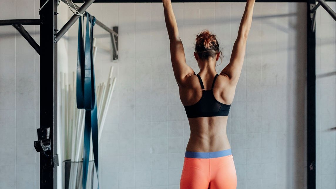 Back view of muscular sportswoman doing pull ups at the gym.