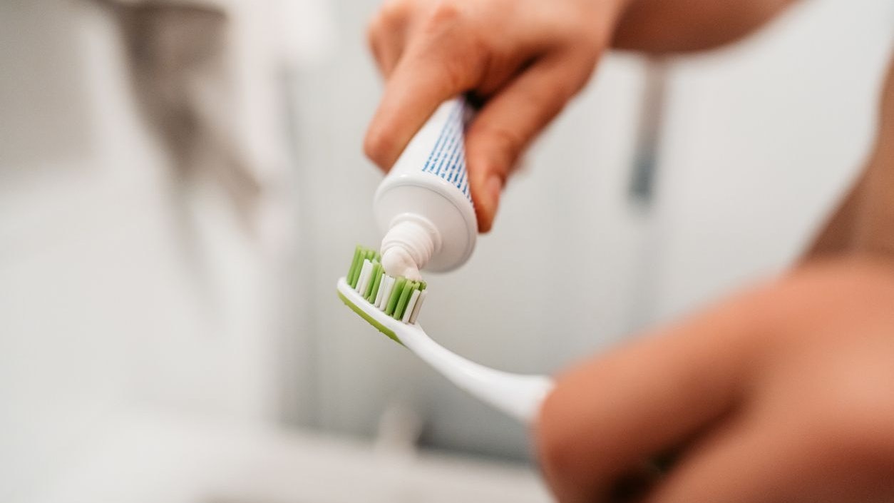 Close-up of a young man putting on toothpaste on a toothbrush to brush his teeth in the bathroom in the morning.