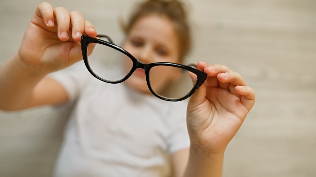 Child girl holding black-framed glasses in her hands. Glasses in focus, the child is blurred. Vision impairment concept