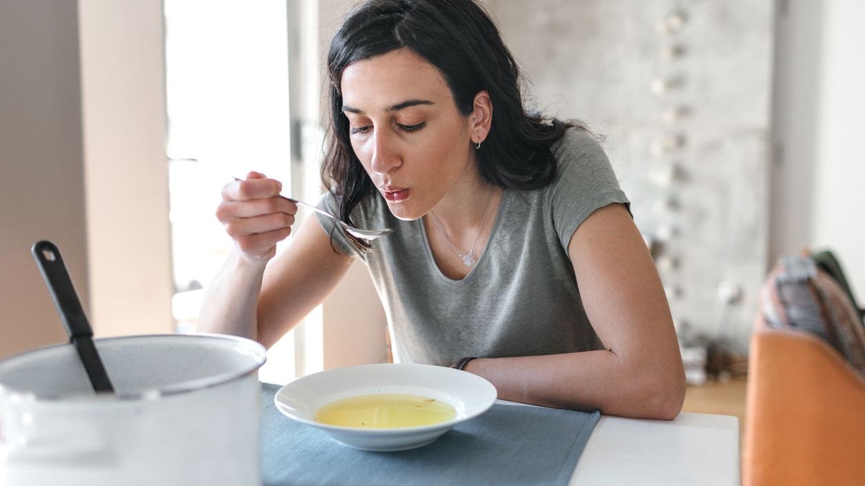 Young woman sick at home eating soup.