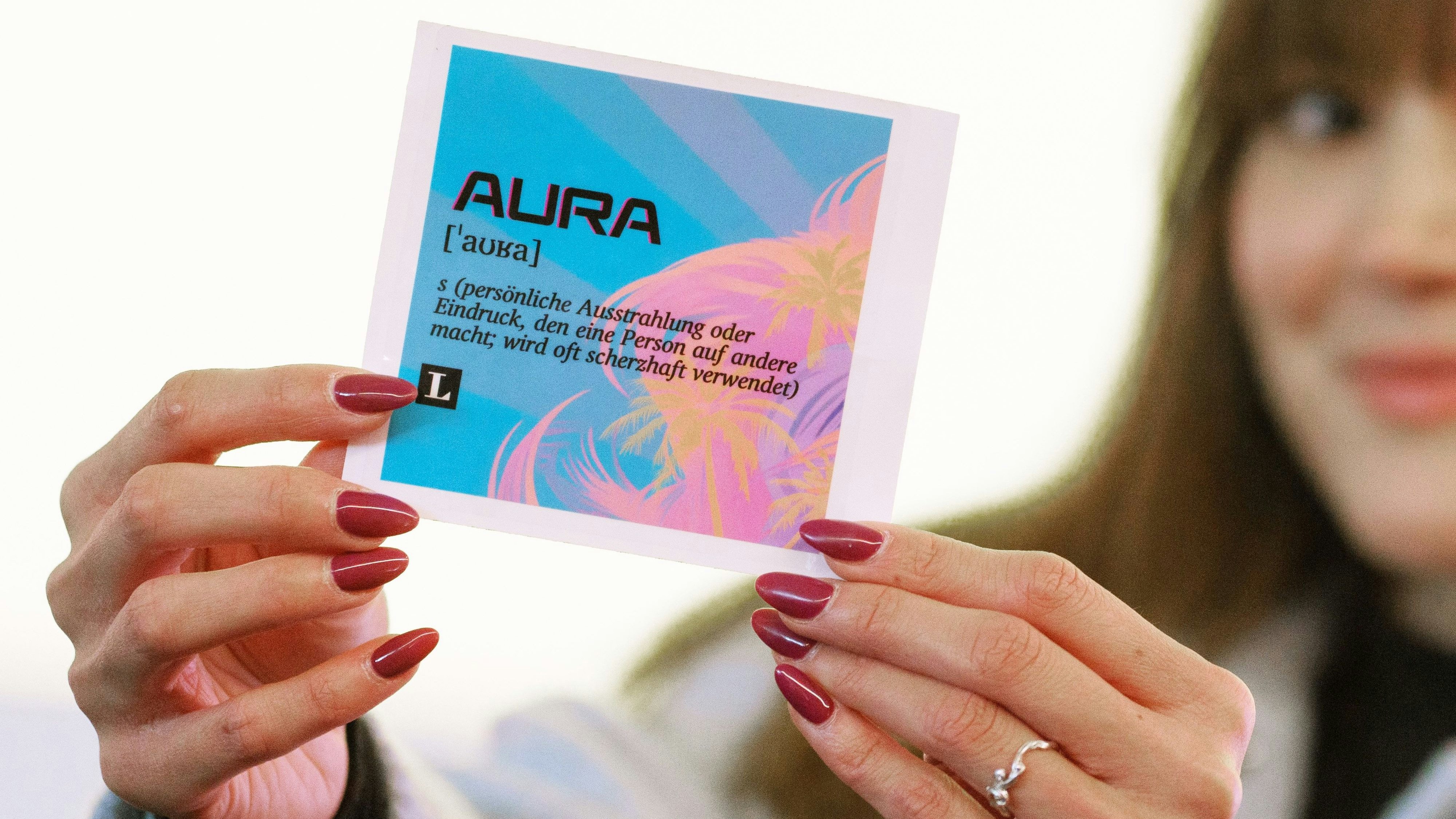 Download von www.picturedesk.com am 19.10.2024 (15:33).  19 October 2024, Hesse, Frankfurt/Main: Patricia Kunth, Project Manager Youth Word / PONS Langenscheidt, holds a sticker with the youth word 2024 "Aura". "Aura" is the youth word of the year 2024. Langenscheidt Verlag has called on young people between the ages of eleven and 20 to submit suggestions for the youth word. Photo: Andreas Arnold/dpa - 20241019_PD2109 - Rechteinfo: Rights Managed (RM)