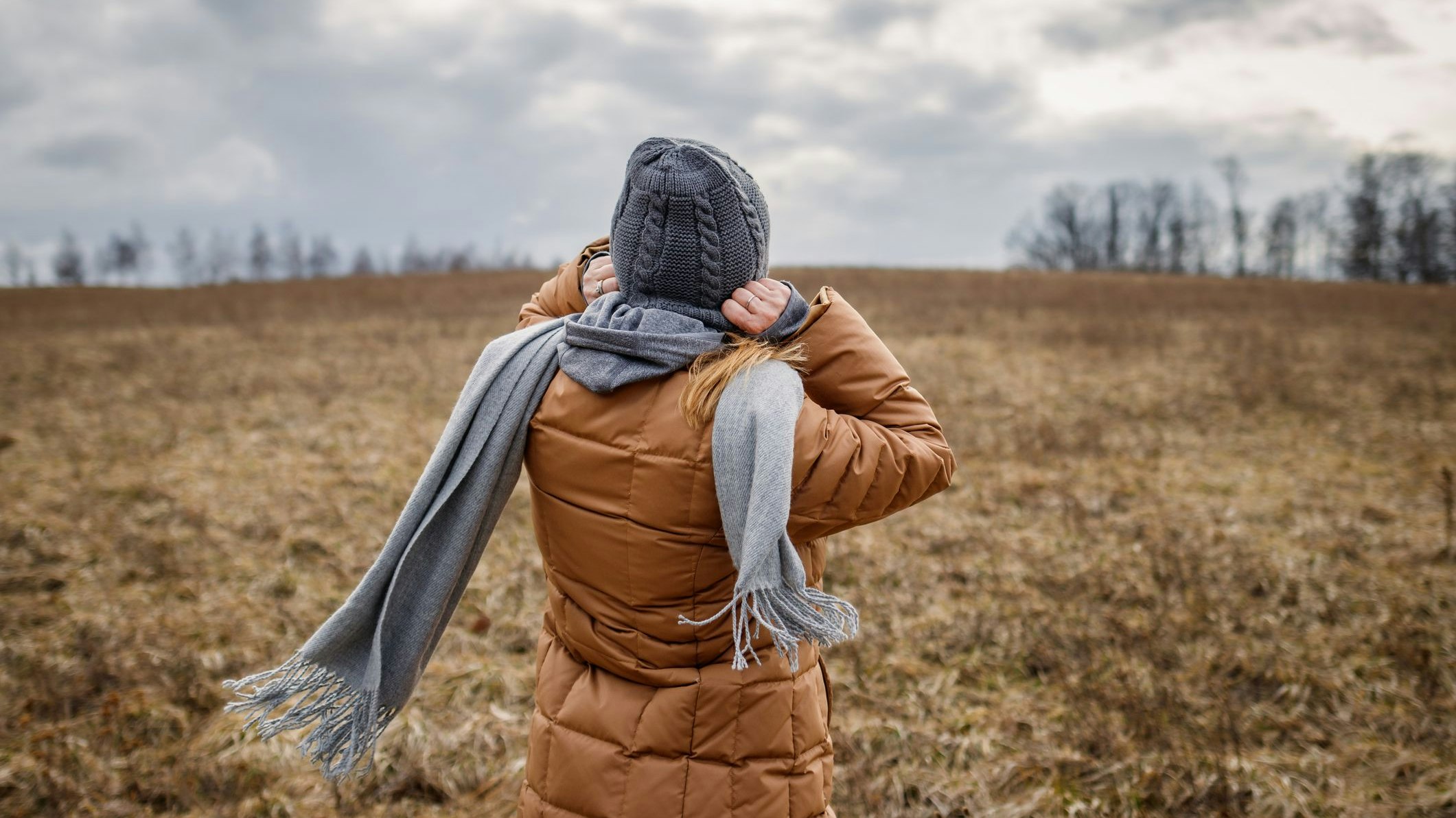 Wind and cold weather. Woman wearing coat, scarf and knit hat outdoors. Female person walks in nature