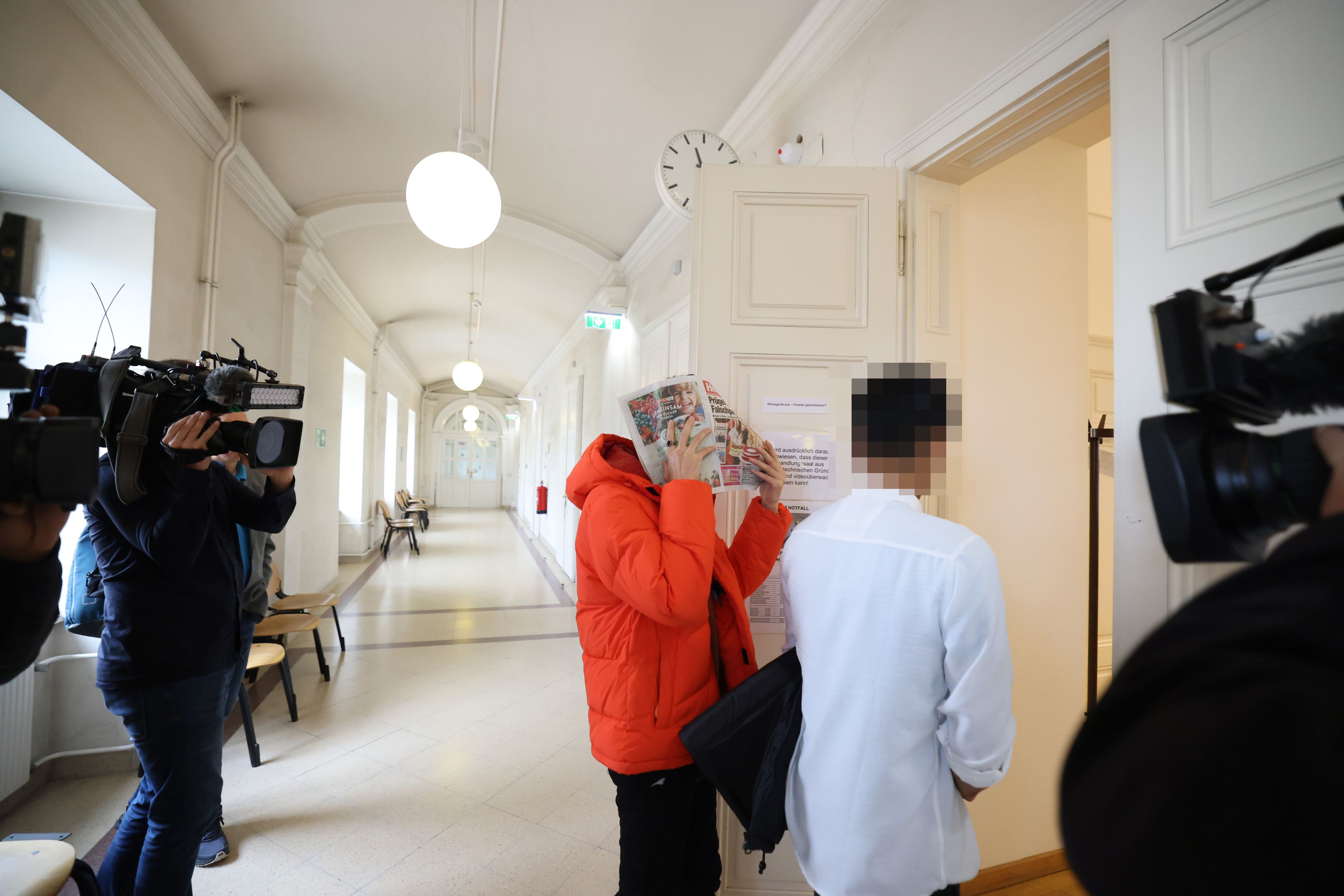 Der Angeklagte (in der orangen Jacke) schütze sein Gesicht mit einer Zeitung vor Gericht; neben ihm ein Zeuge, der die 14-Jährige ebenfalls getroffen hatte.