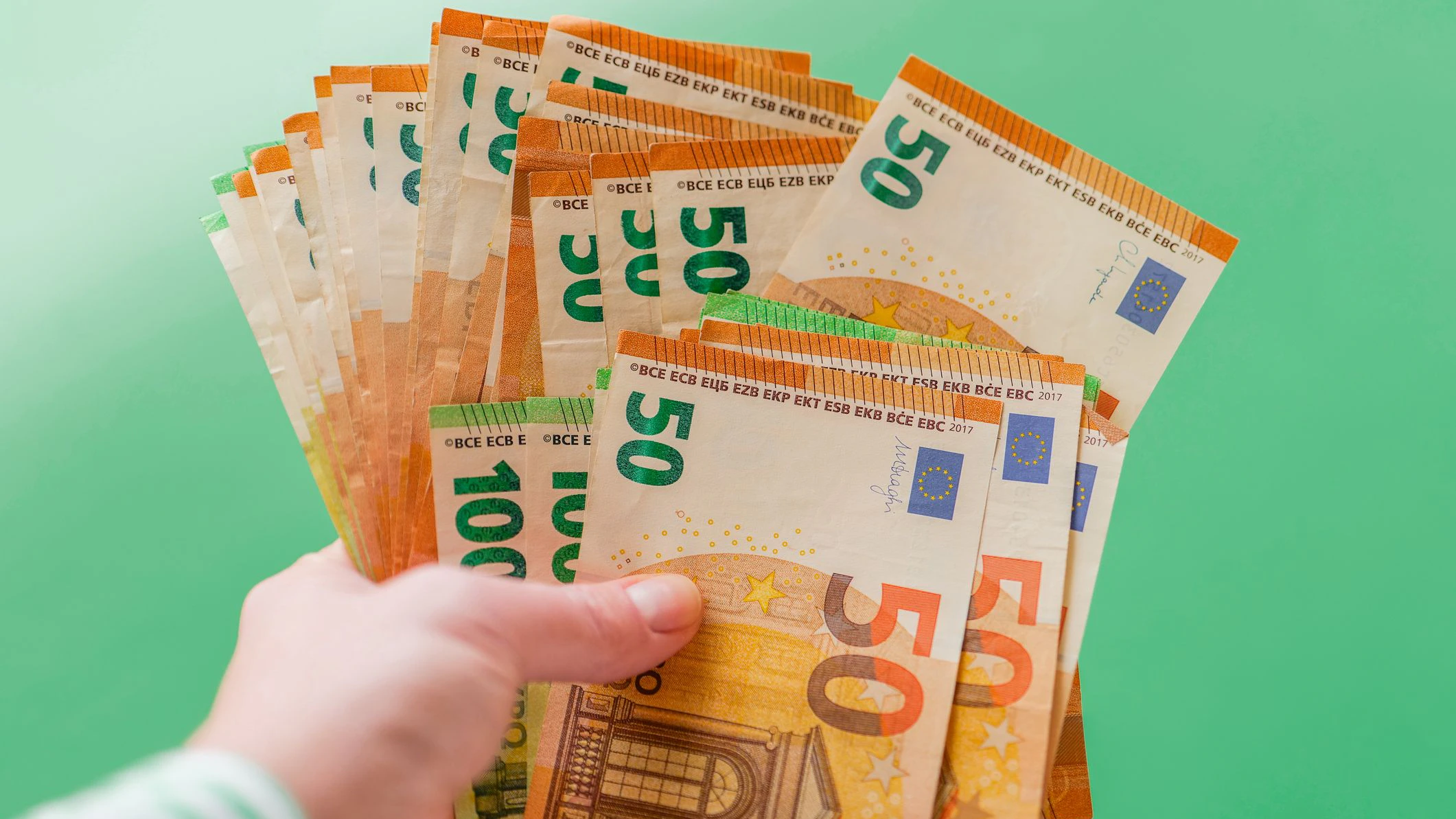 Euro money.Benefits, subsidies, wages and pensions in Europe.Hand in striped blouse holding euro bills fan on green background. One hundred euro bills pack.