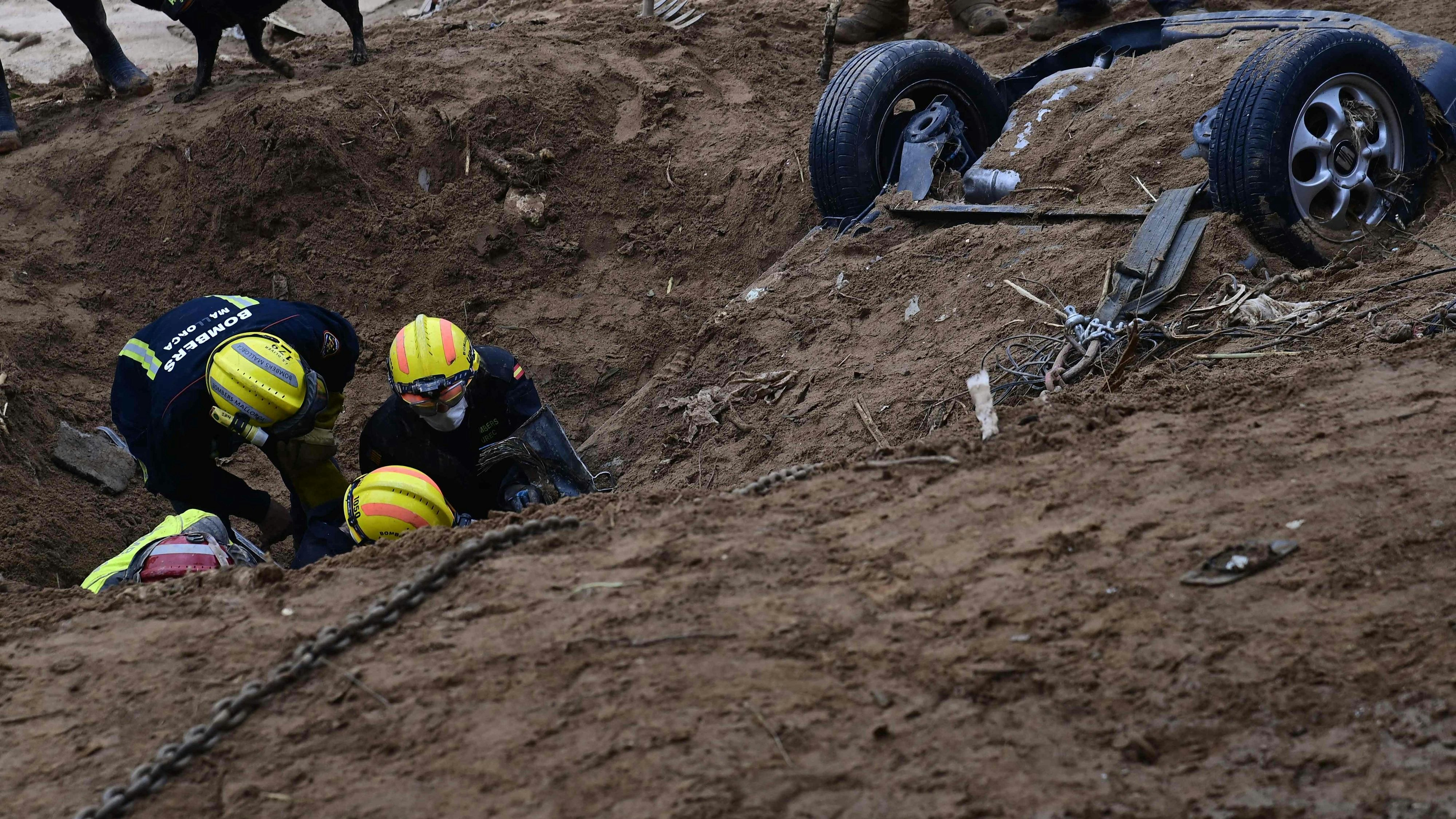 Feuerwehrleute graben in Paiporta bei Valencia einen Wagen aus, der am Ufer eines Flusses vollkommen verschüttet worden ist