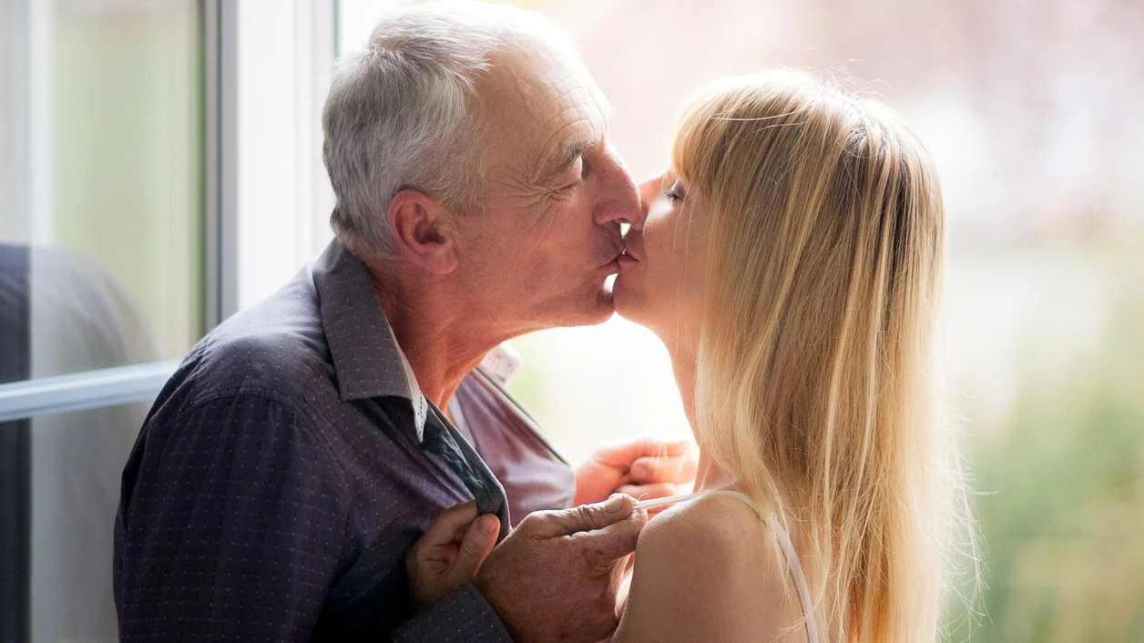 Lovely Couple with Age Difference Kissing near Opened Window inside the House During Summer Time