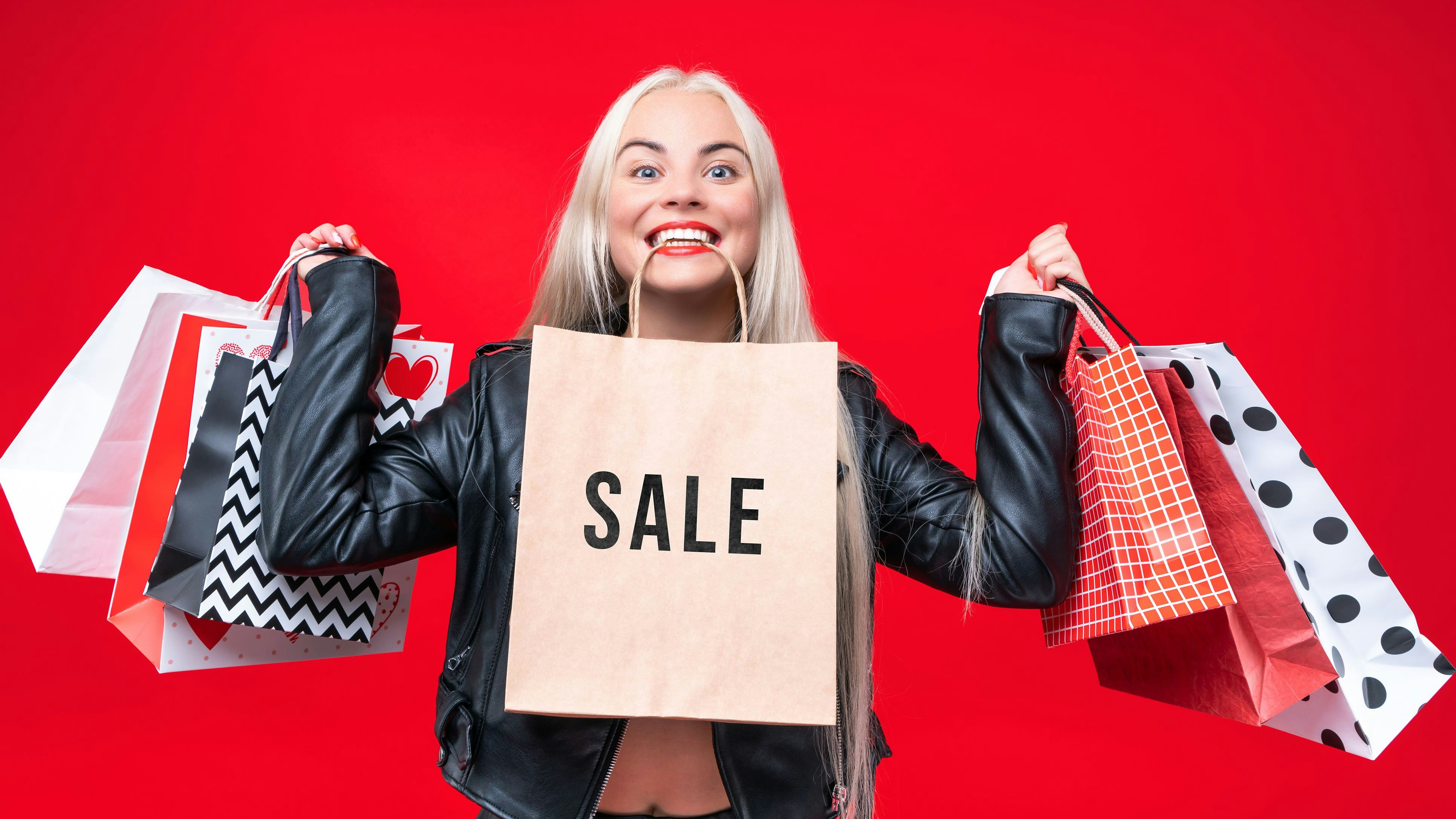 Happy woman consumer in black dress with shopping bags isolated on a red background. Black Friday and Sale concept