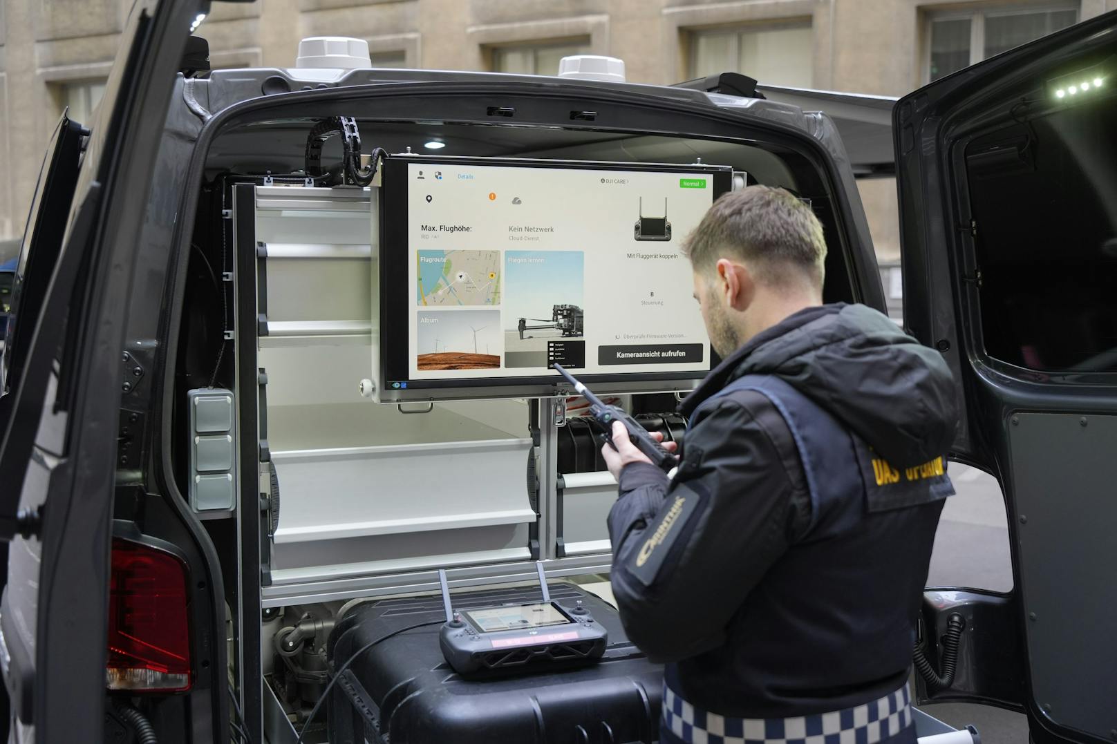 Bildschirm im Einsatzfahrzeug zeigt Flugdaten und Position der Drohne, ein Polizist bereitet den Einsatz vor.