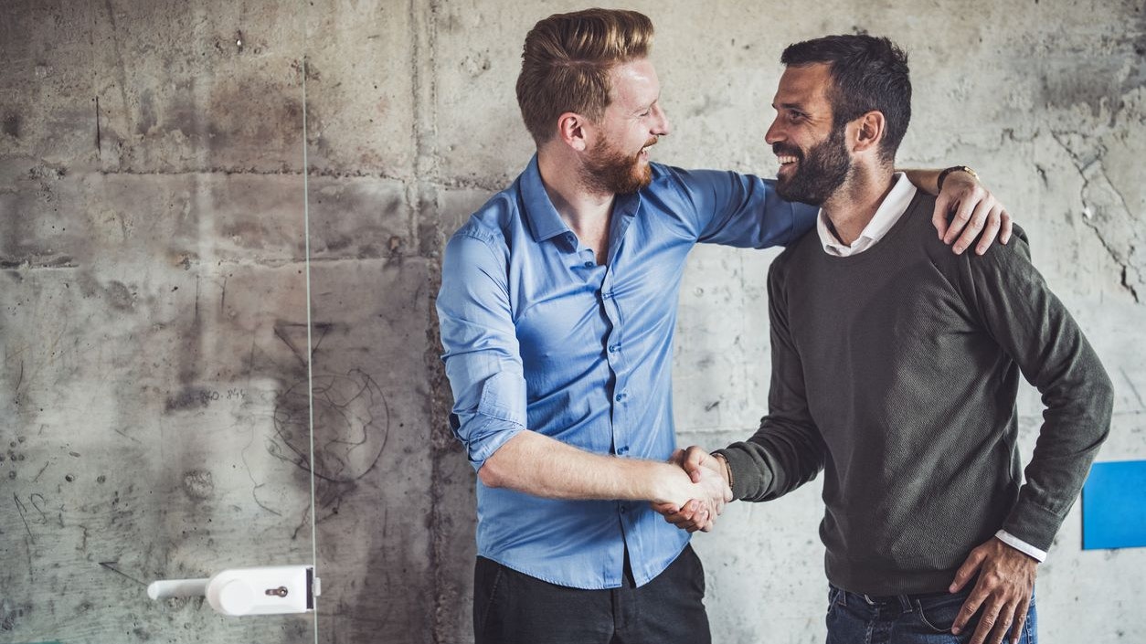 Young happy businessmen talking while shaking hands in the office.