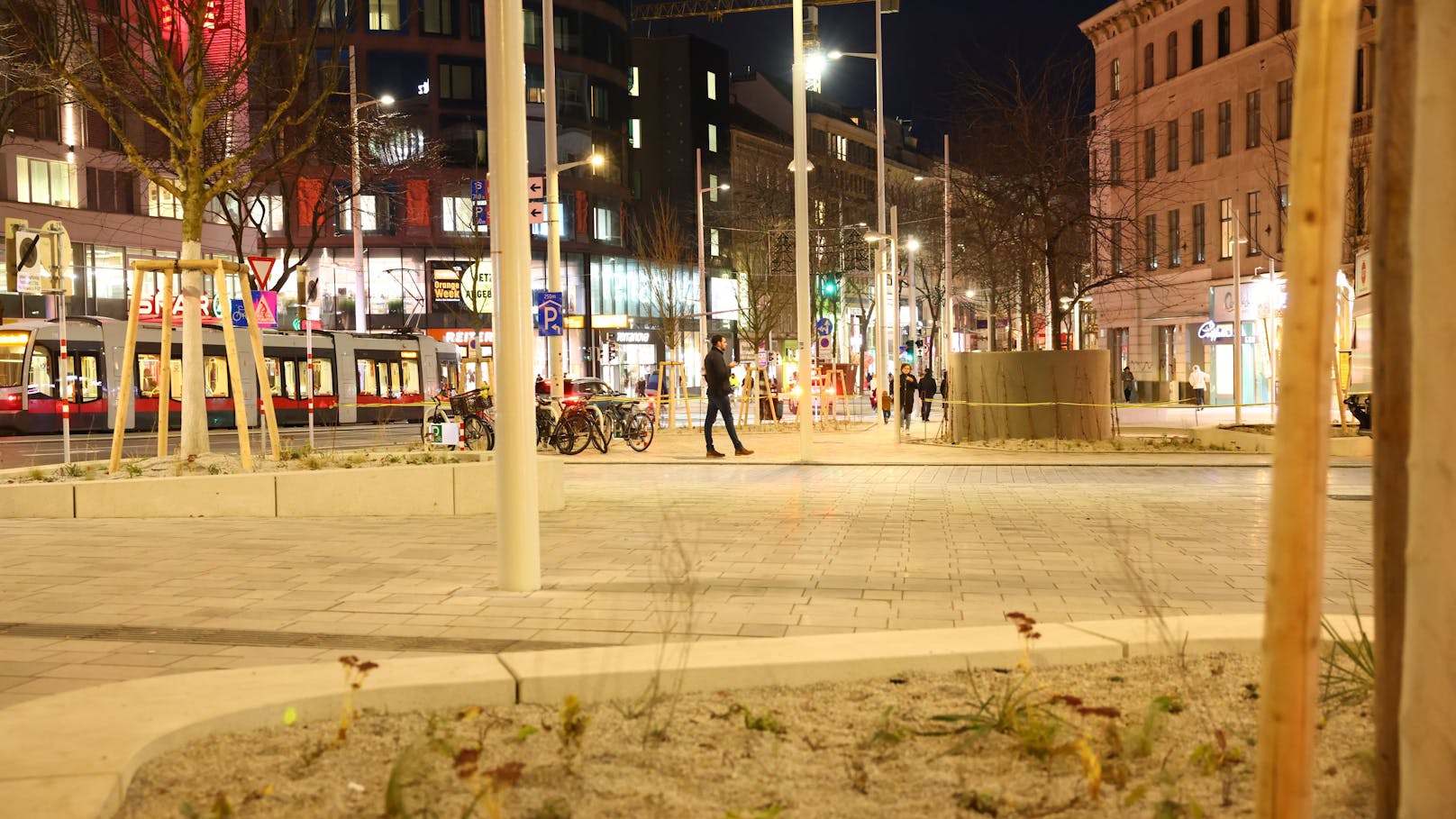 Der Broda-Platz bei Nacht: Geschäfte und Passanten beleben die neu gestaltete Umgebung, während Sicherheitsfragen weiterhin im Fokus stehen.