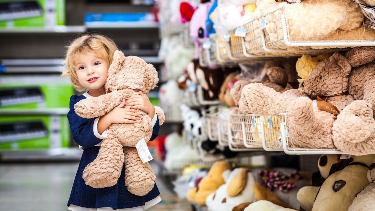 Pretty smiling little girl with teddy-bear in grocery store