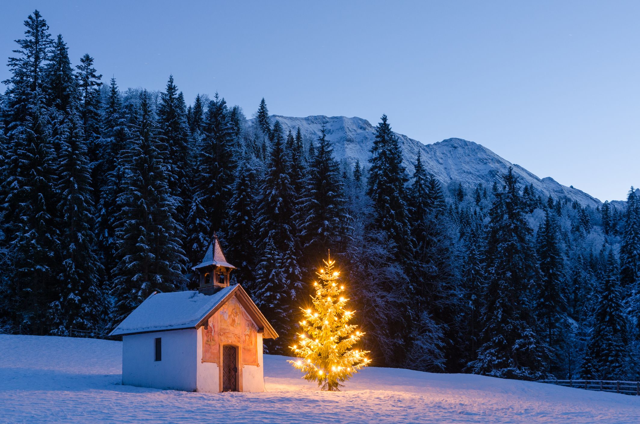 Eine weihnachtlich beleuchtete Kapelle in schneebedeckter Winterlandschaft.