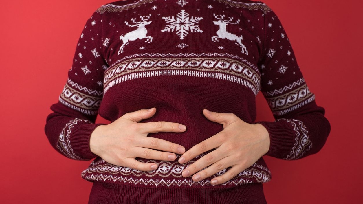 Cropped closeup photo of girl in red and white christmas sweater holding her hurting stomach on isolated red background
