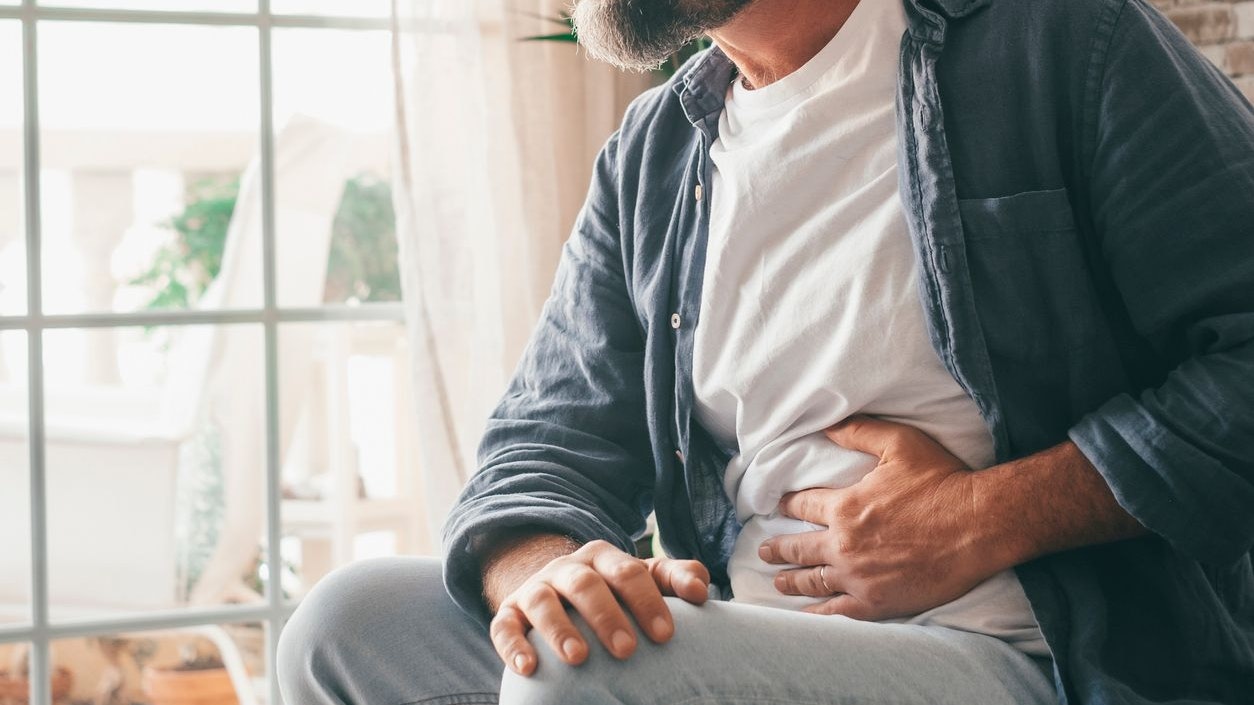 Man suffering with severe stomach pain sitting at home. Hand of mature guy holding abdomen suffering from ache, diarrhea or indigestive problem. Caucasian guy pressing on belly on painful sensation