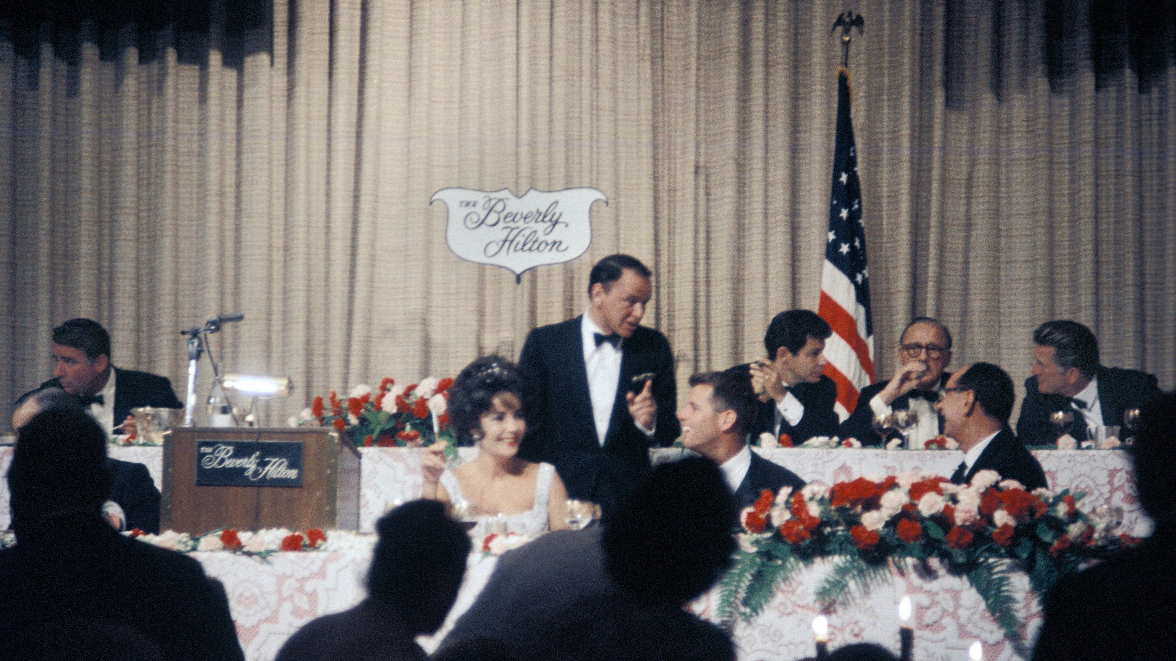 Gemeinsame Benefizveranstaltung 1961 mit den Kennedys im Beverly Hilton in Los Angeles:Peter Lawford (am Podium ganz links), Elizabeth Taylor, Frank Sinatra, Robert F. Kennedy (rechts neben Sinatra), Eddie Fisher, Jack Benny und Kirk Douglas alle am Podium)