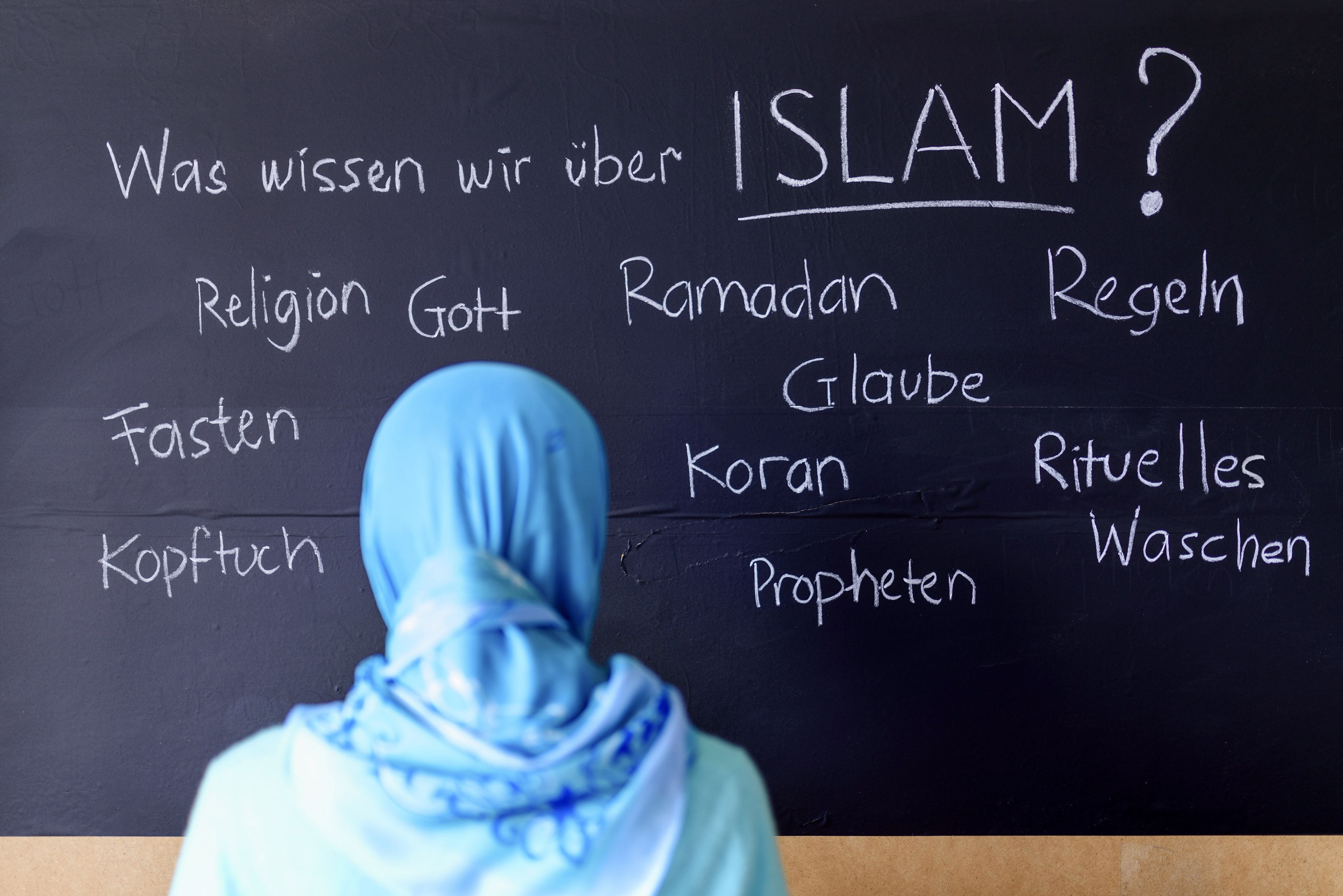 Eine muslimische Schülerin vor einer Tafel mit Begriffen aus dem Islam im Islamunterricht. (Themenbild, Symbolbild) 