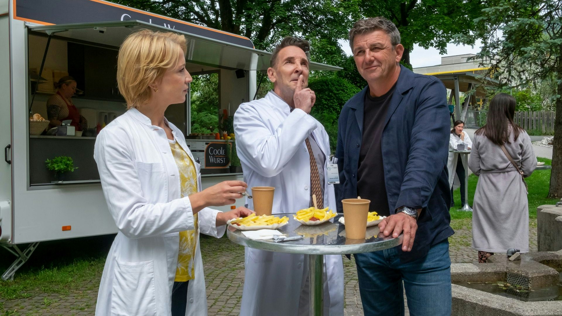Dr. Alexander Kahnweiler (Mark Keller, M.) sucht eine neue Herausforderung und teilt seine Idee mit Dr. Angelika Rüdiger (Annika Ernst, l.) und Dr. Martin Gruber (Hans Sigl, r.).