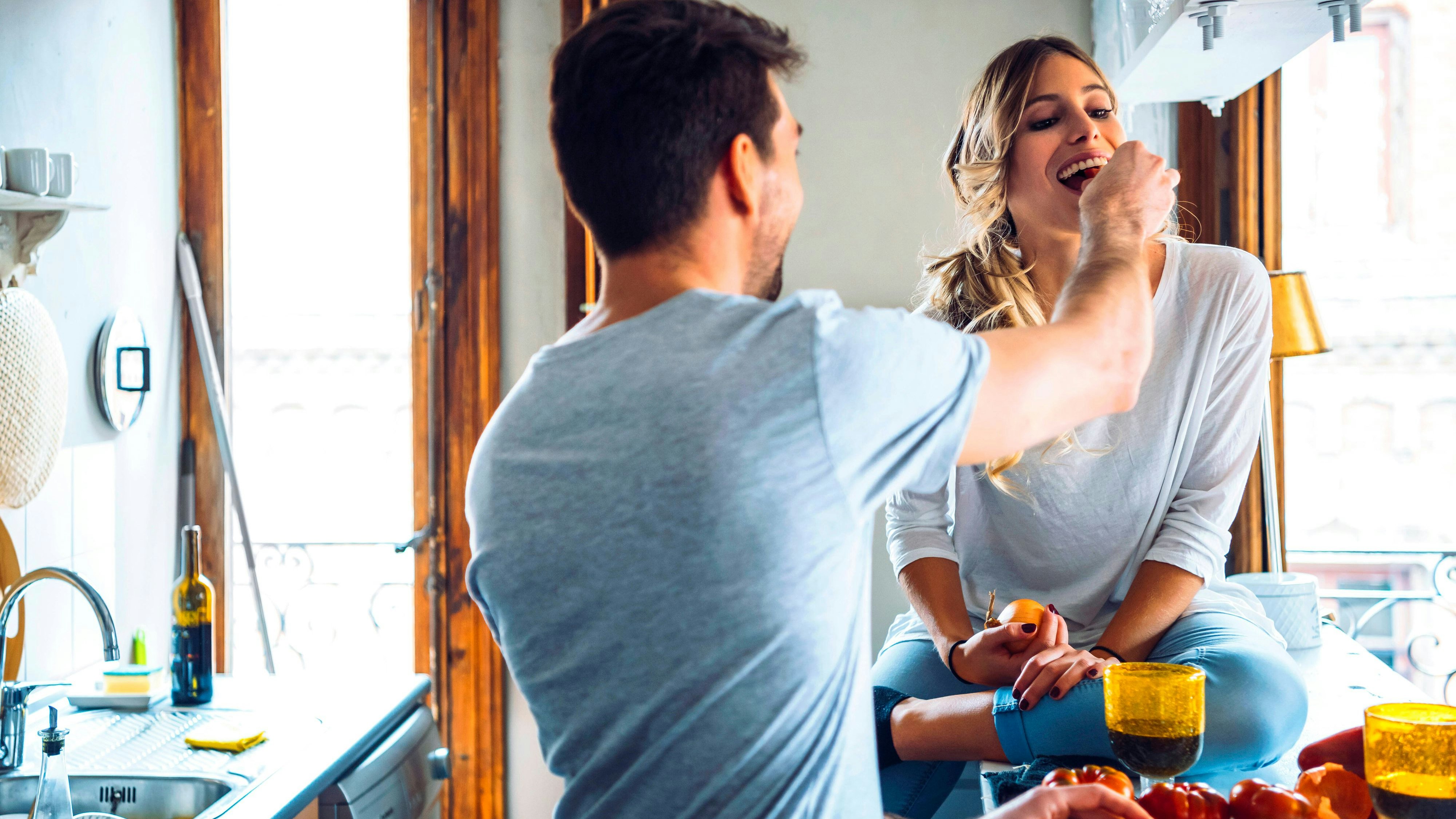 Young man preparing food and feeding girlfriend in kitchen at home model released Symbolfoto property released EHF00933 
