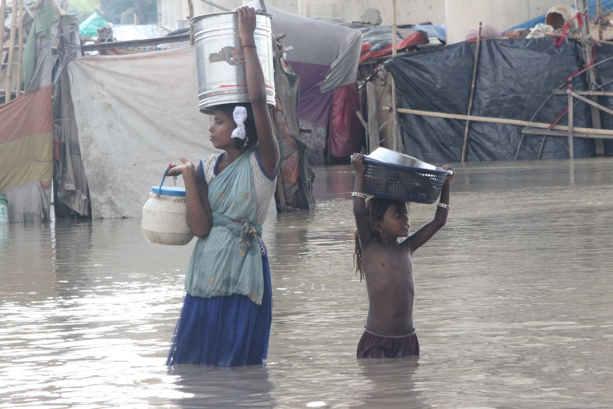 Mädchen und junge Frauen tragen ihre Habseligkeiten durch die Fluten eines Hochwassers.