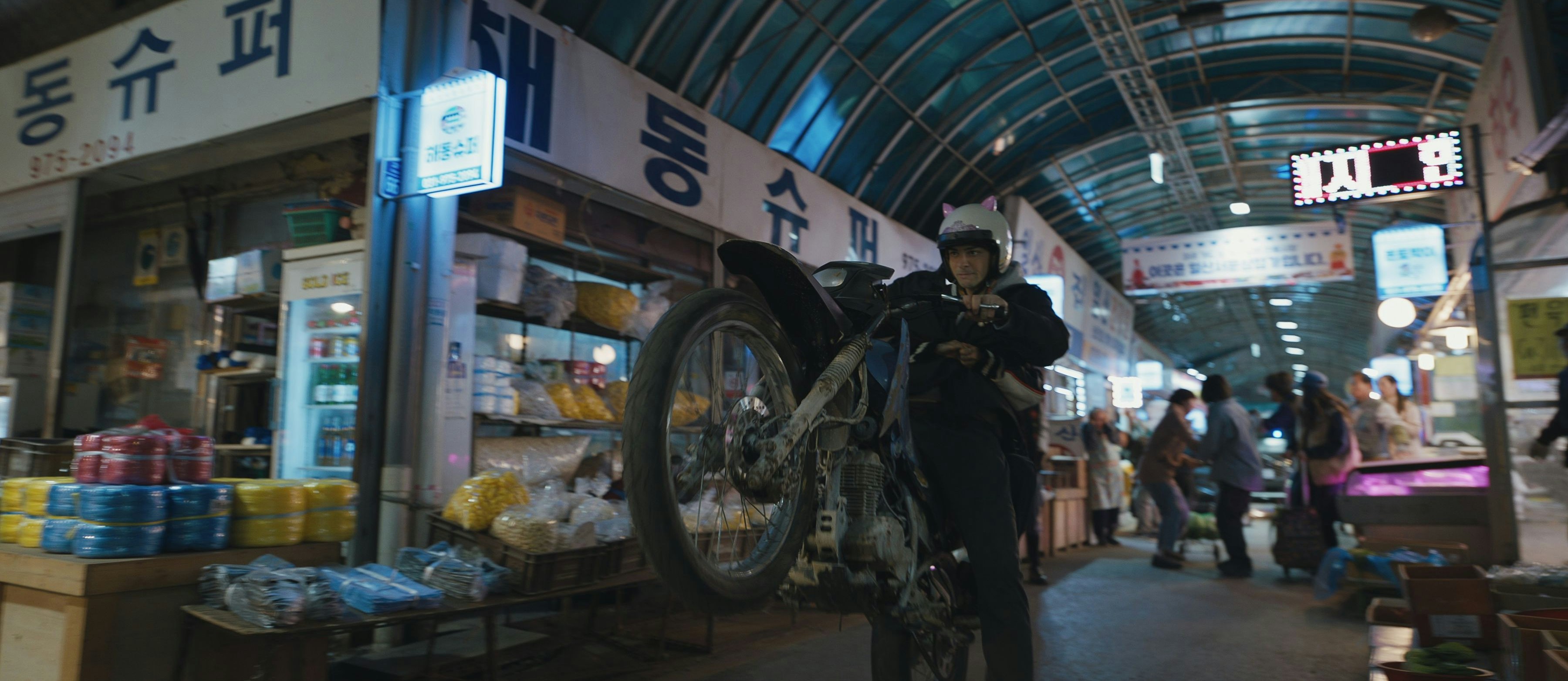 Und hoch das Rad! Noah Centineo als CIA-Mitarbeiter Owen Hendricks beim unorthodoxen Cruisen durch einen Indoor-Markt in Seoul: "The Recruit", Staffel 2, auf Netflix