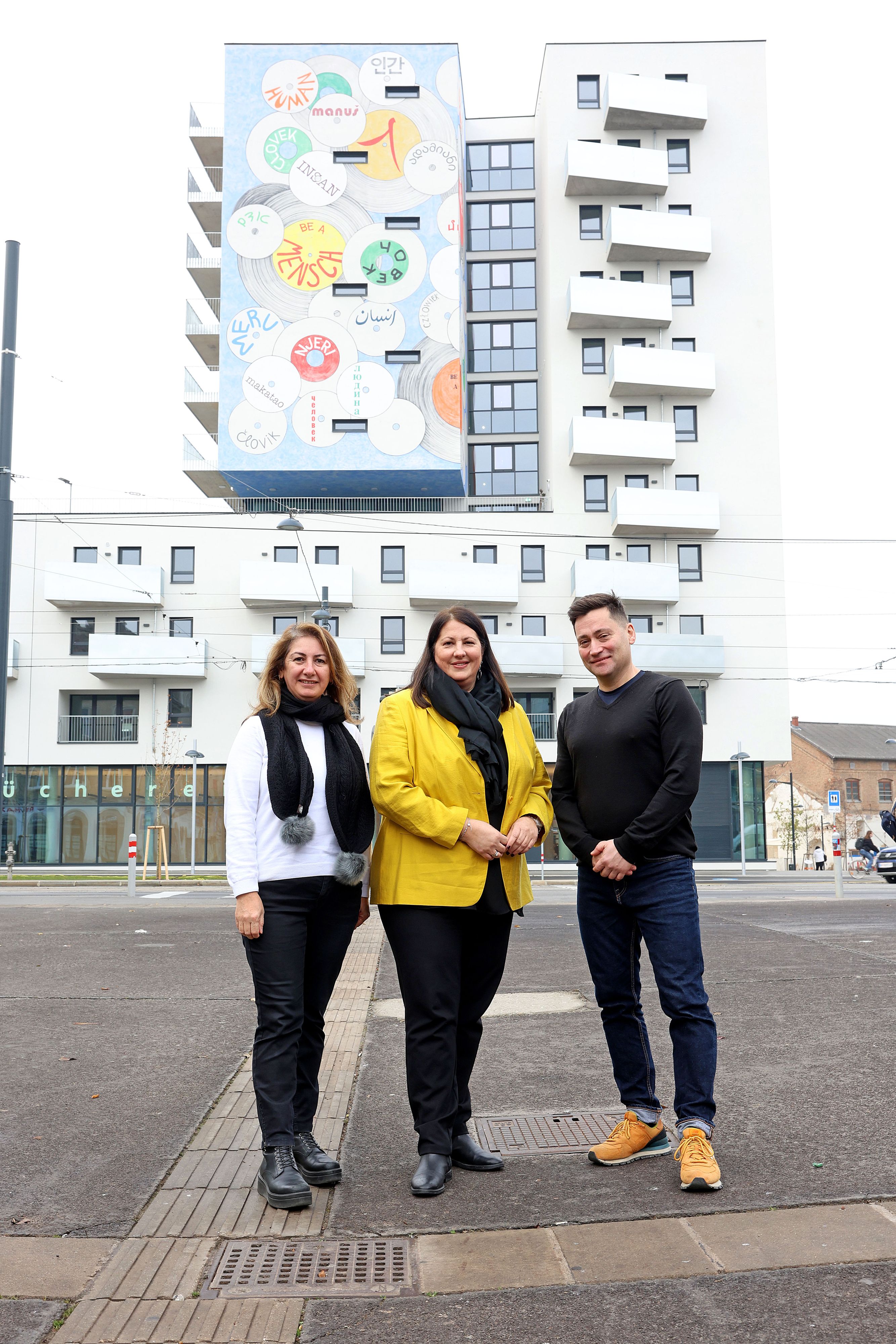 Ebru Ayas und Burak Büyük vom Nachbarschaftsservice wohnpartner mit Vizebürgermeisterin und Wohnbaustadträtin Kathrin Gaál vor dem neuen Gemeindebau an der Laxenburger Straße.