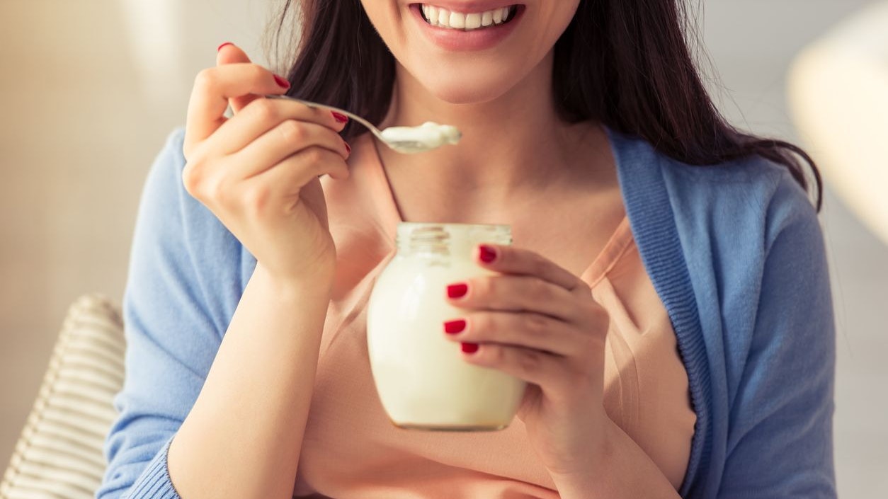Cropped image of beautiful pregnant woman eating yogurt and smiling while sitting at home