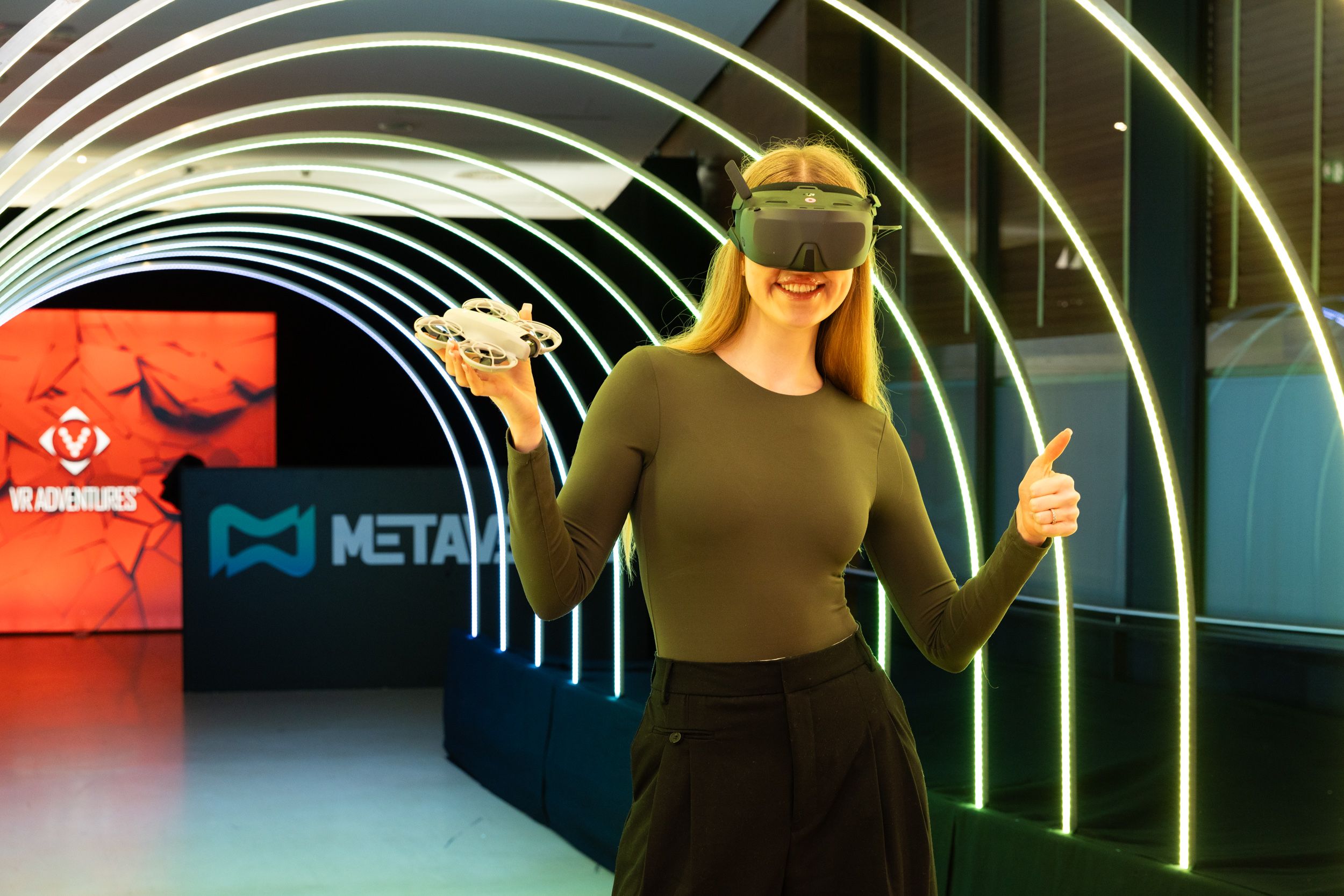 Eine Besucherin des Metaverse Vienna zeigt ihre Drohne und genießt das VR-Erlebnis inmitten der futuristischen Lichtinstallation.